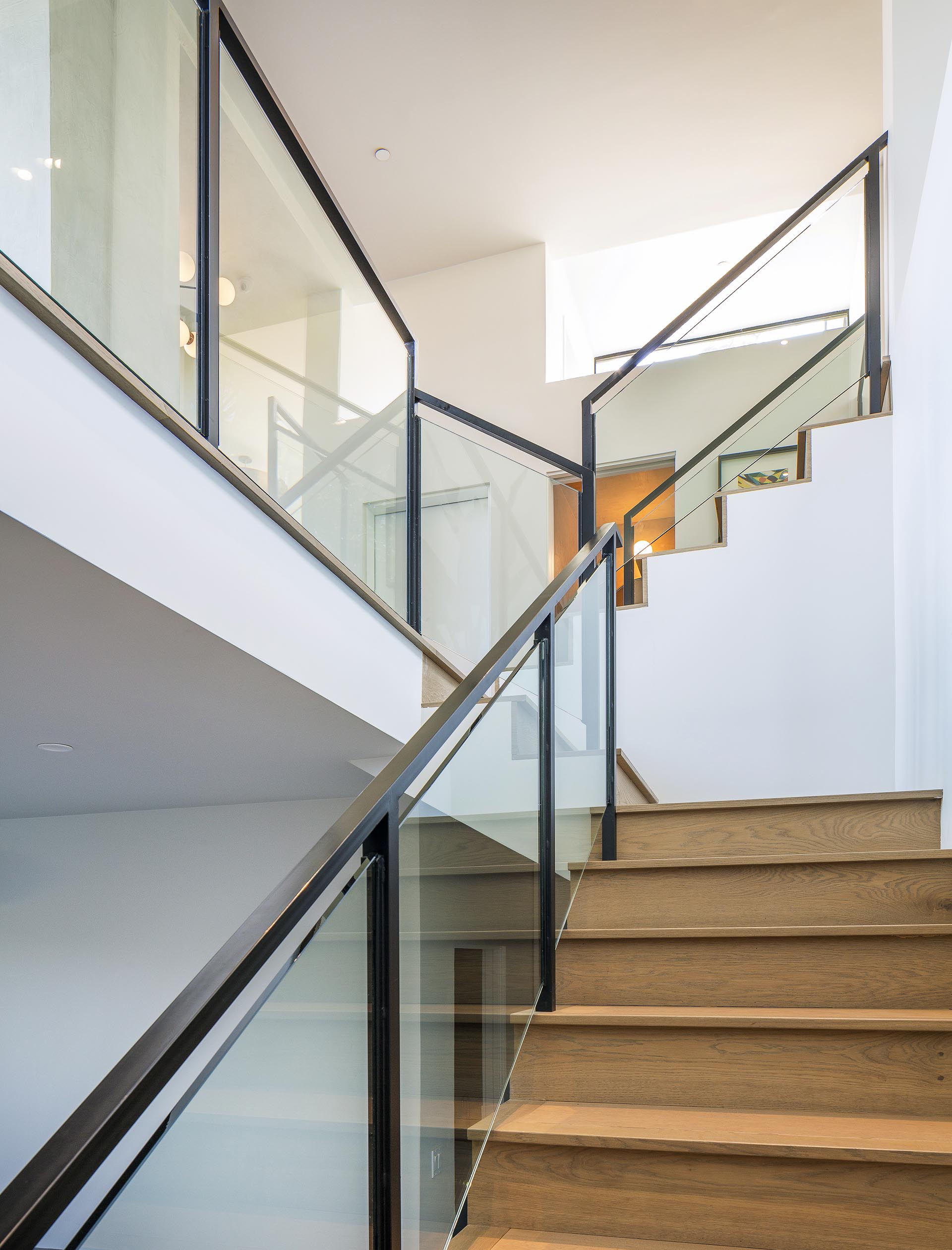 Connecting the various levels of this modern house are wood stairs that have a glass and metal railing.