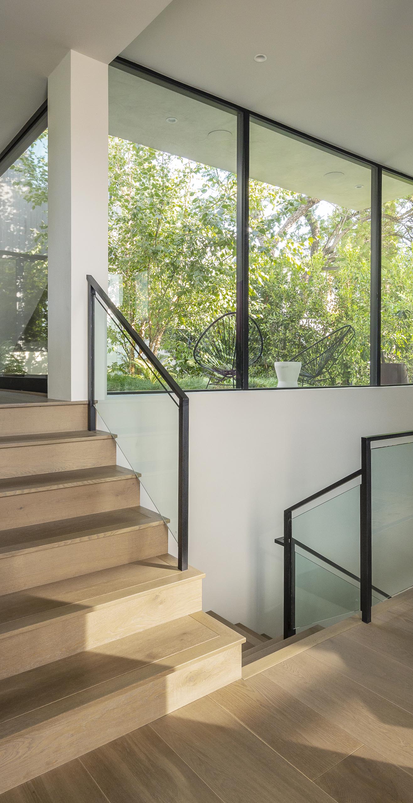 Connecting the various levels of this modern house are wood stairs that have a glass and metal railing.