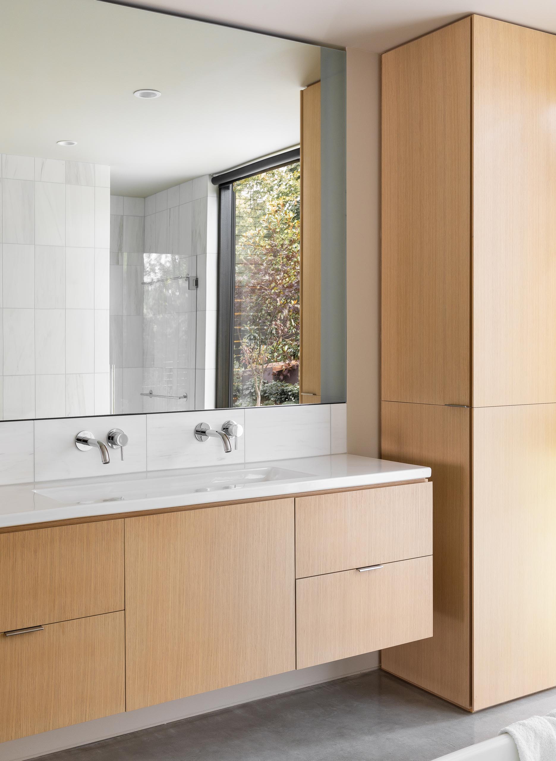 In this modern master bathroom, there's a dual sink vanity and wood cabinets, while on the opposite wall, there's a freestanding bathtub and shower.