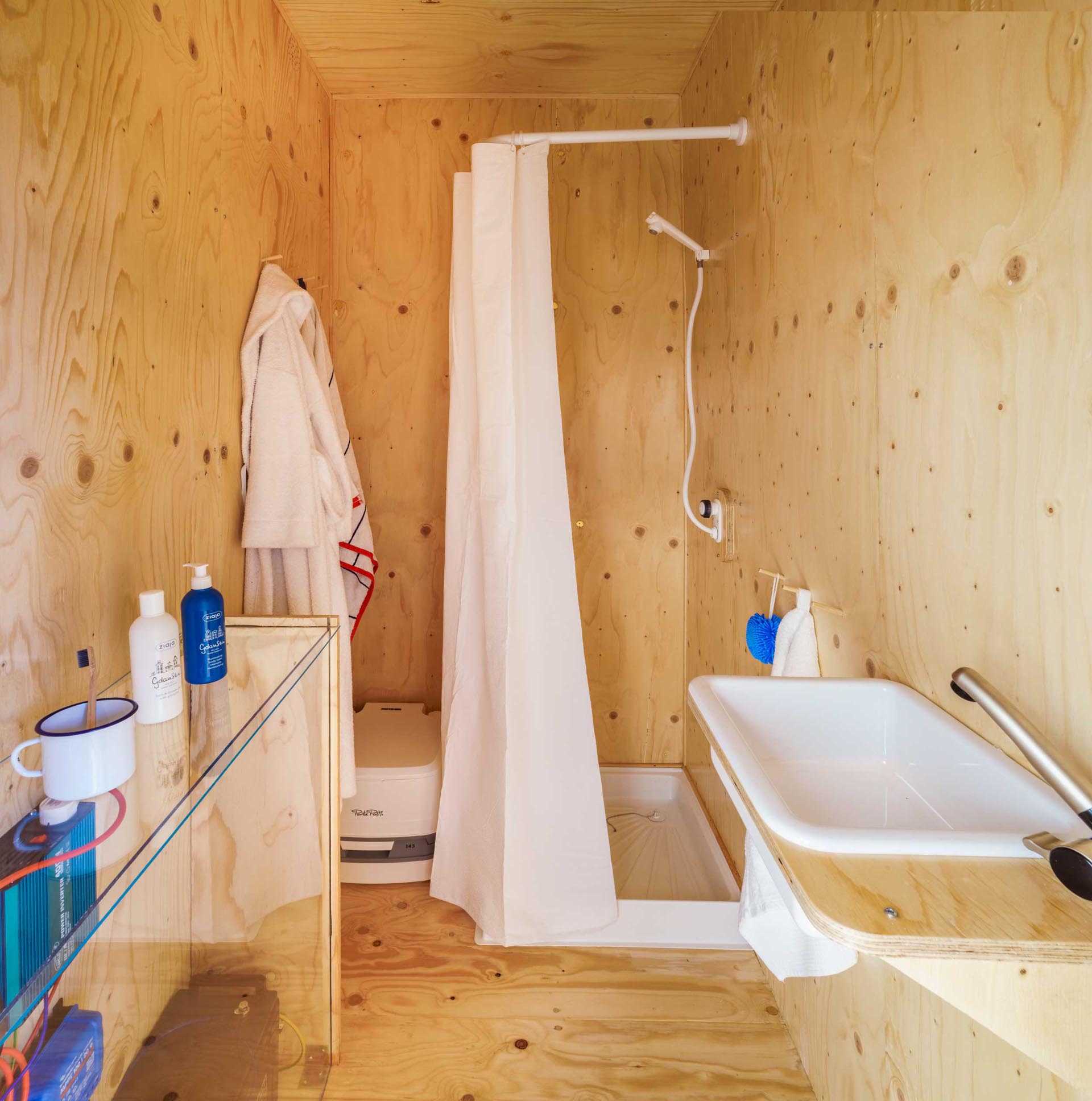 A tiny home made from a shipping container has a plywood lined bathroom with a shower.