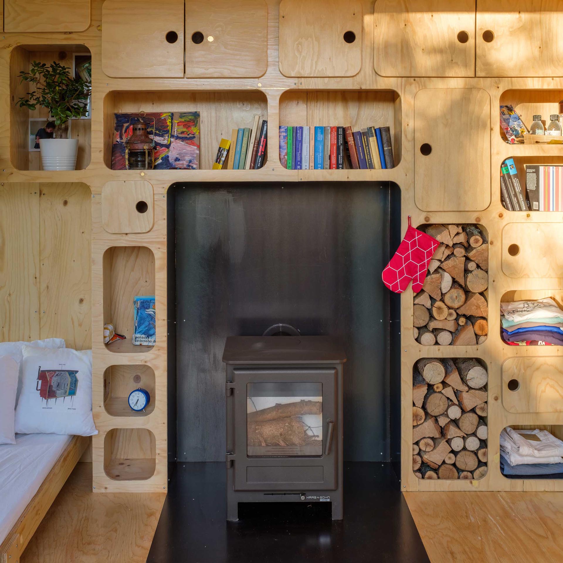 A tiny home made from a shipping container has a fold-down bed, plenty of storage cabinets, and a fireplace.