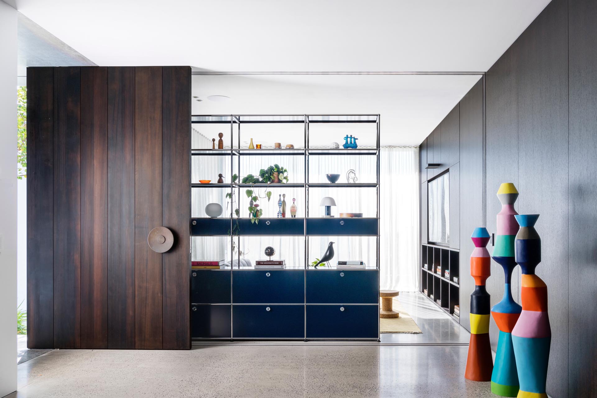 An oversized floor-to-ceiling dark pivoting timber front door welcomes guests to this modern home.