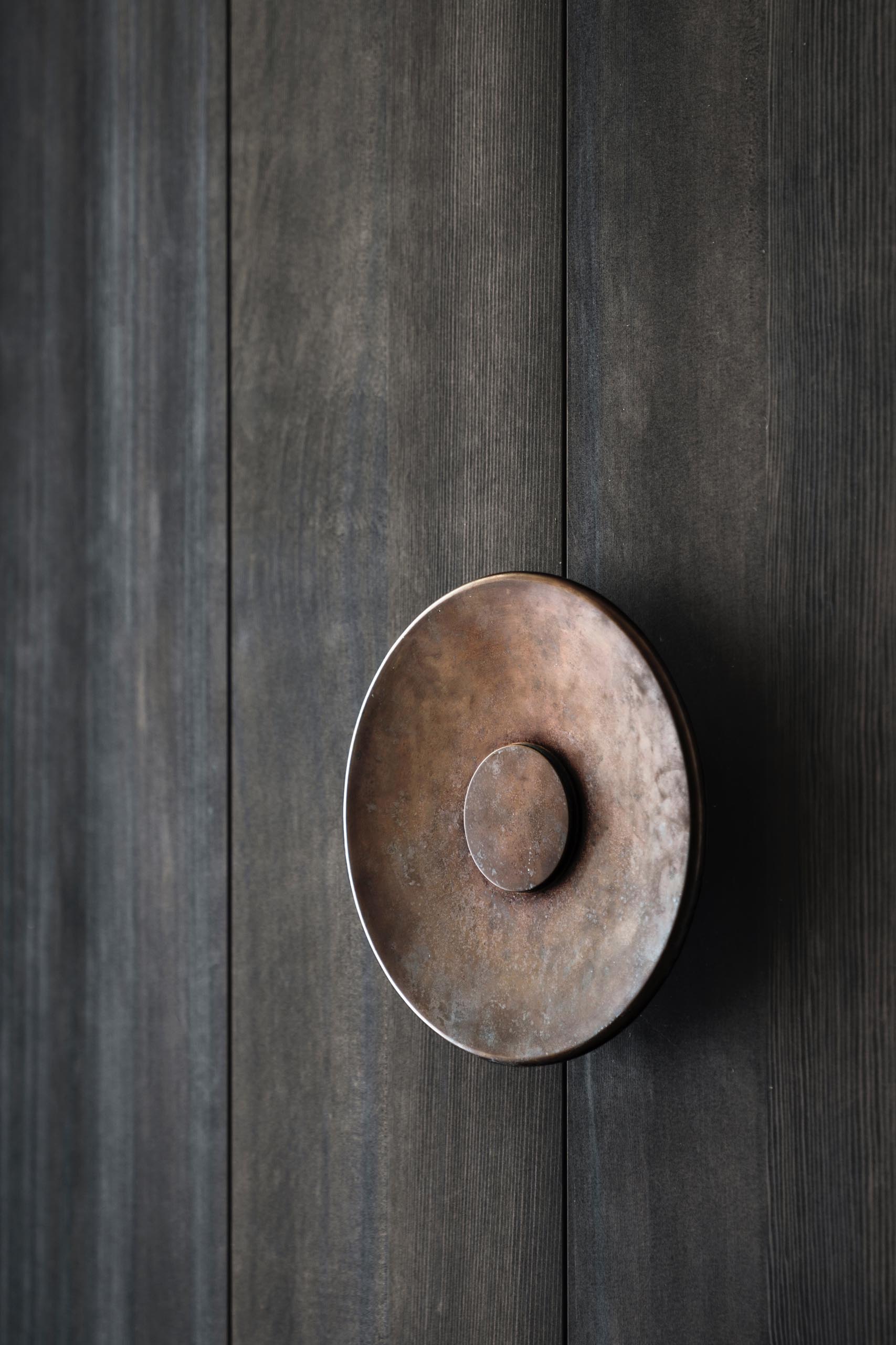 An oversized metal door handle for a large floor-to-ceiling pivoting wood front door.