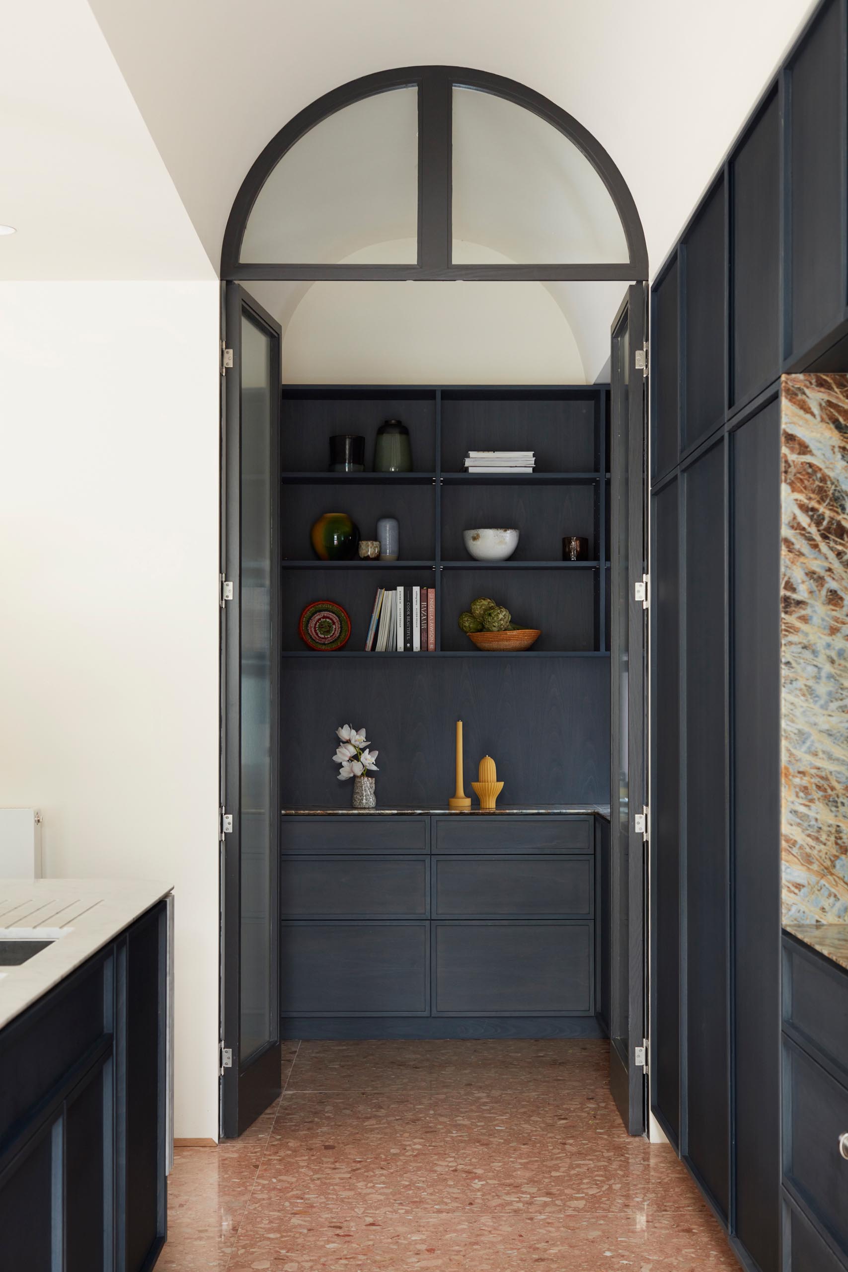 A walk-in pantry with dark cabinets, that's enclosed behind a pair of doors.