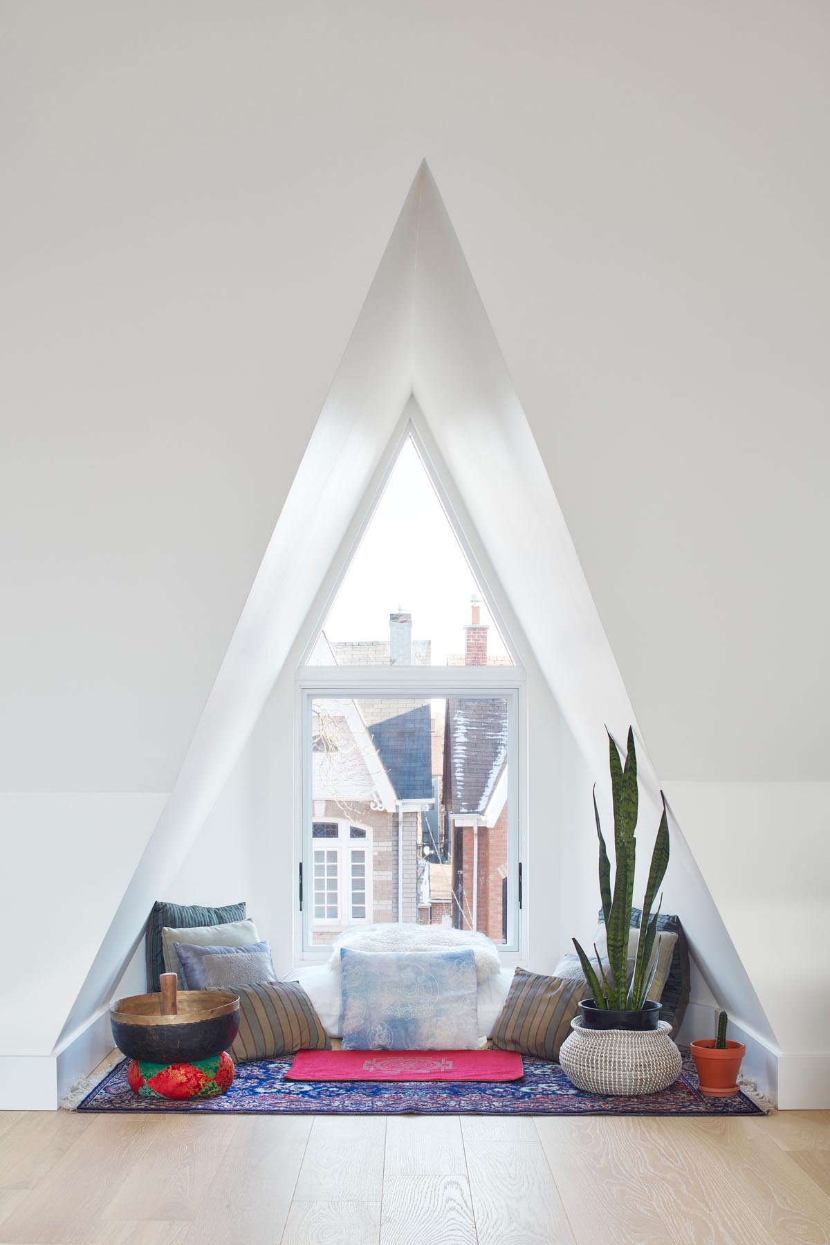 A triangular window nook that been furnished with a rug, plenty of pillows, plants, and a meditation bowl.