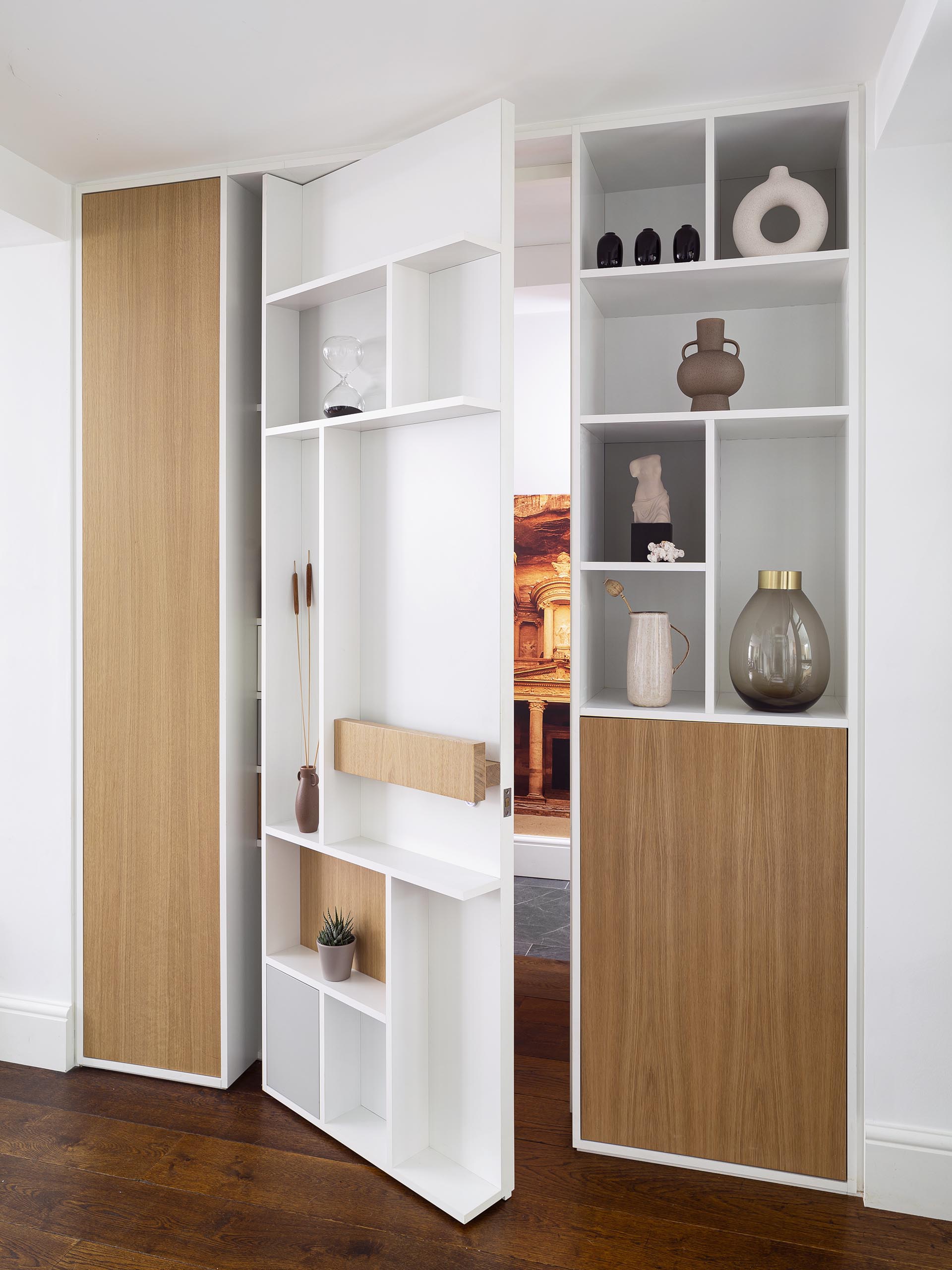 This pivoting door which sits flush with the surrounding shelves and has a simple wood handle that matches the other wood details, and simply swings open to reveal the bathroom.