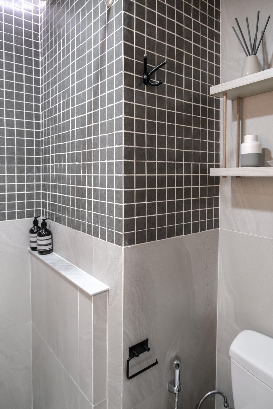 In this small bathroom, large tiles cover the lower half of the walls, while the upper half is covered in square gray tiles.