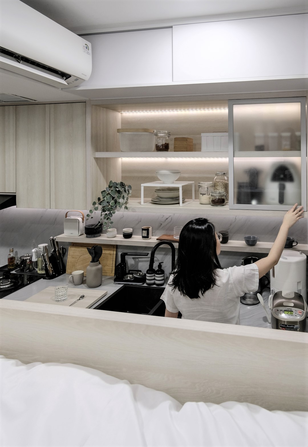 Phòng bếp chung cư nhỏ, được thiết kế với tủ gỗ sáng màu, có dải đèn LED chiếu sáng giúp không gian luôn sáng sủa.