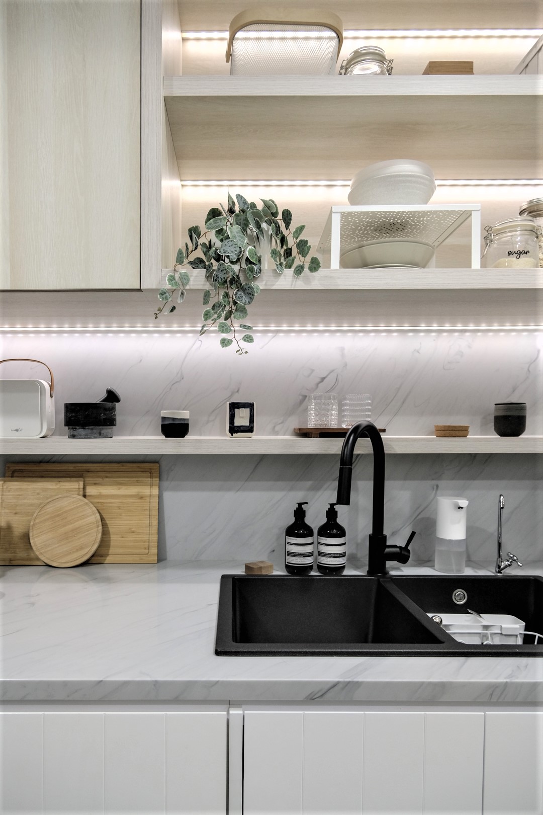 A small apartment kitchen, designed with light wood cabinets, has strips of LED lighting that keeps the space bright.