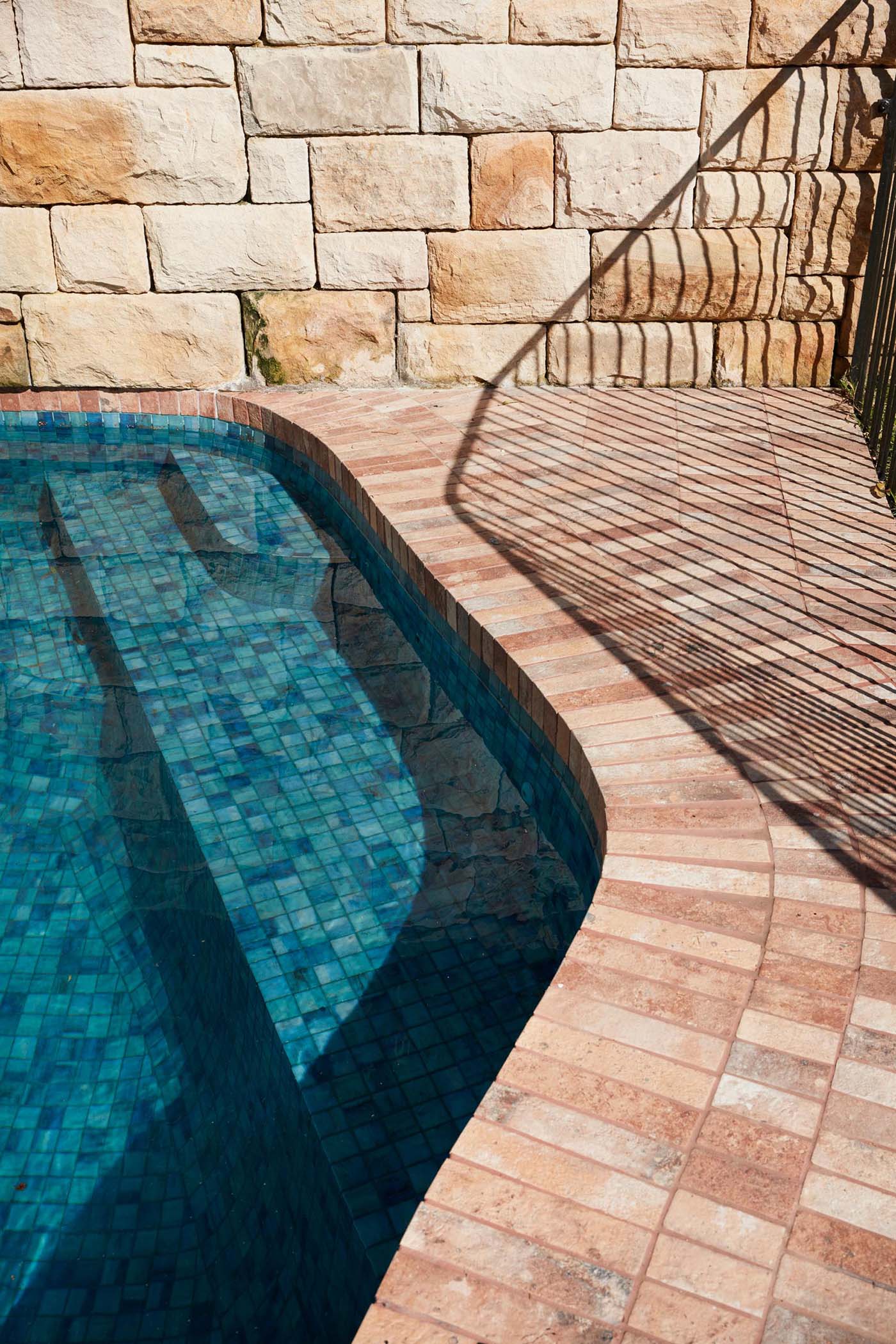 A contemporary pool with brick patio and sandstone wall.