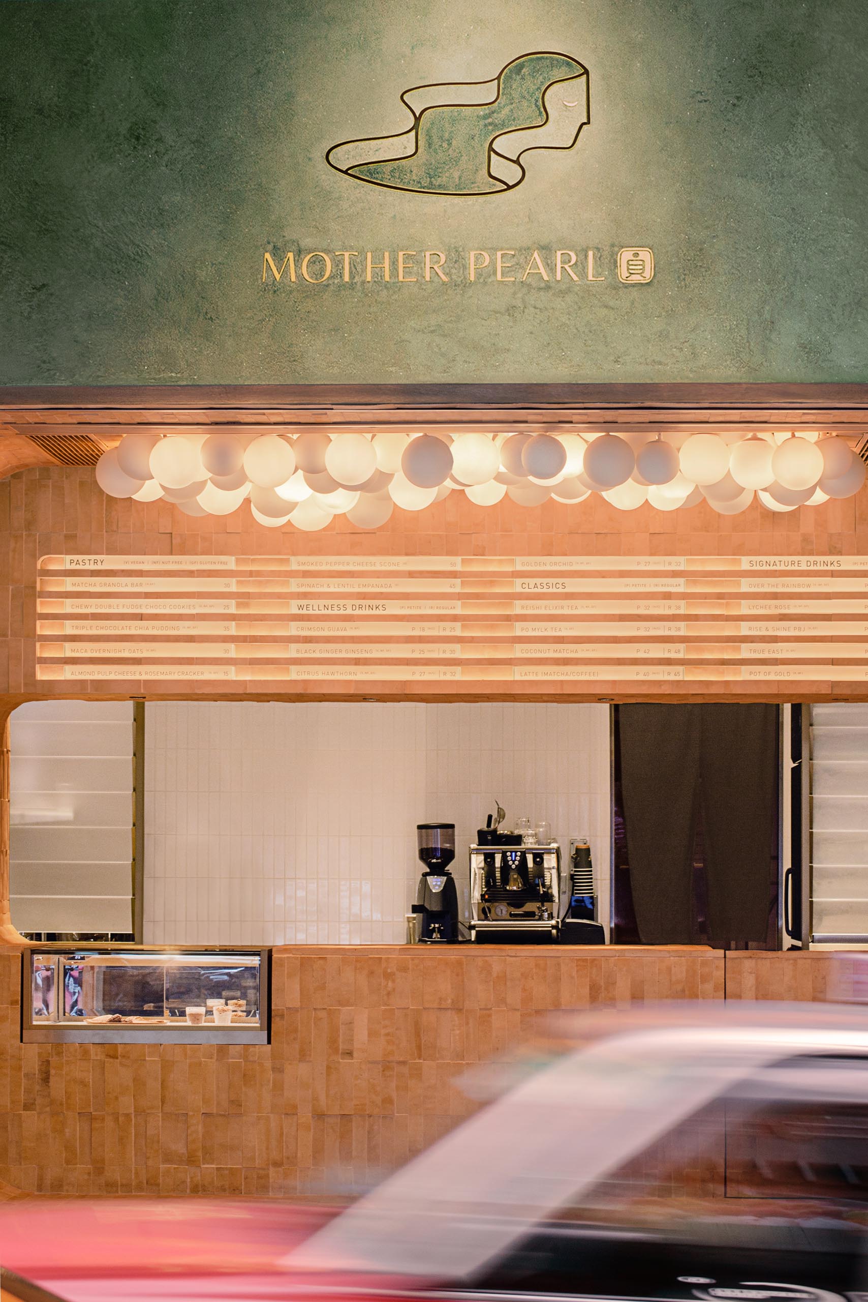 The dark olive green exterior of this tea house stands out against the other shops in the area, with the logo highlighted on the facade.