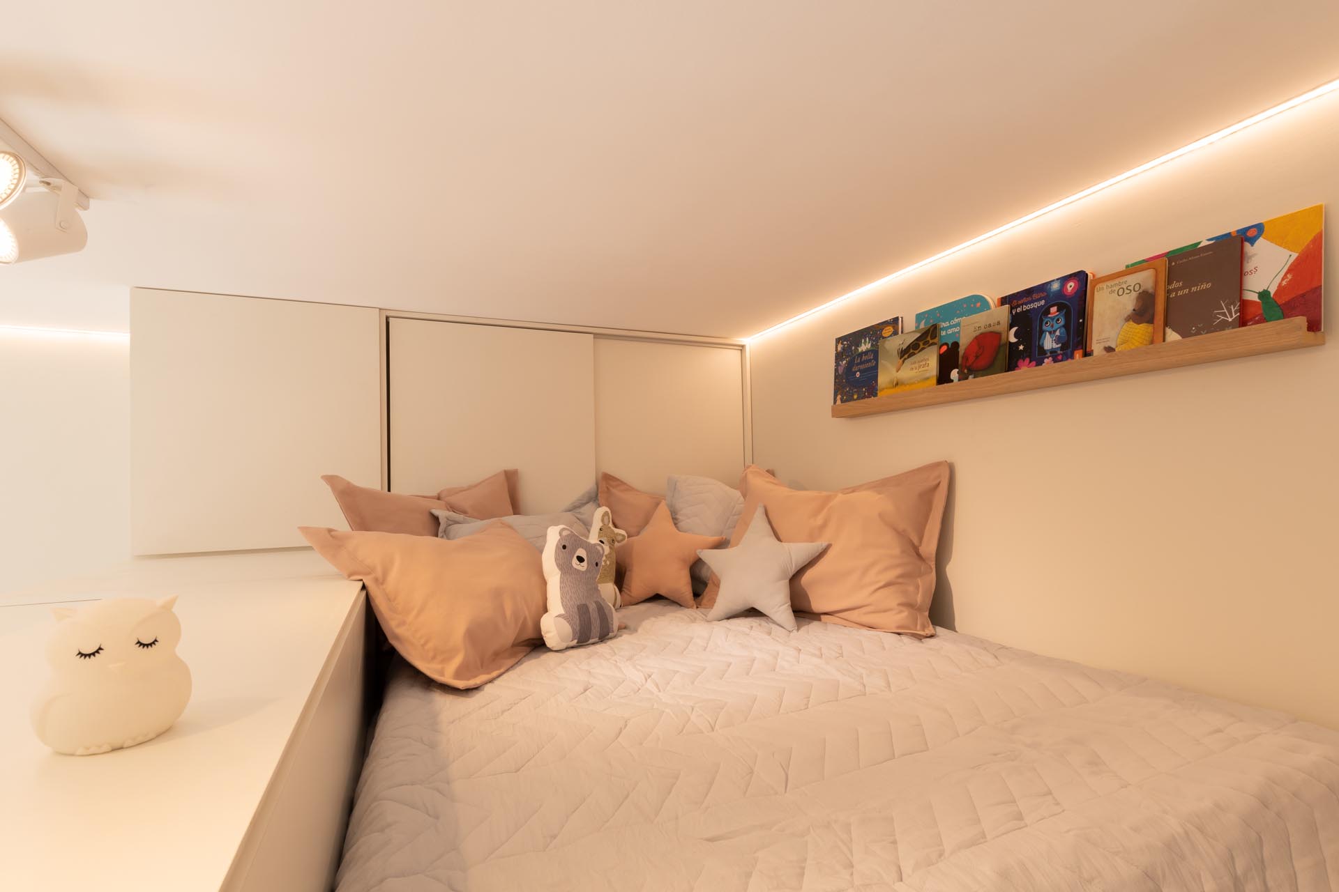 A tiny home with a children's loft bedroom that includes a little storage cabinet at the head of the bed, while a small wood ledge is perfect for storing a few books.