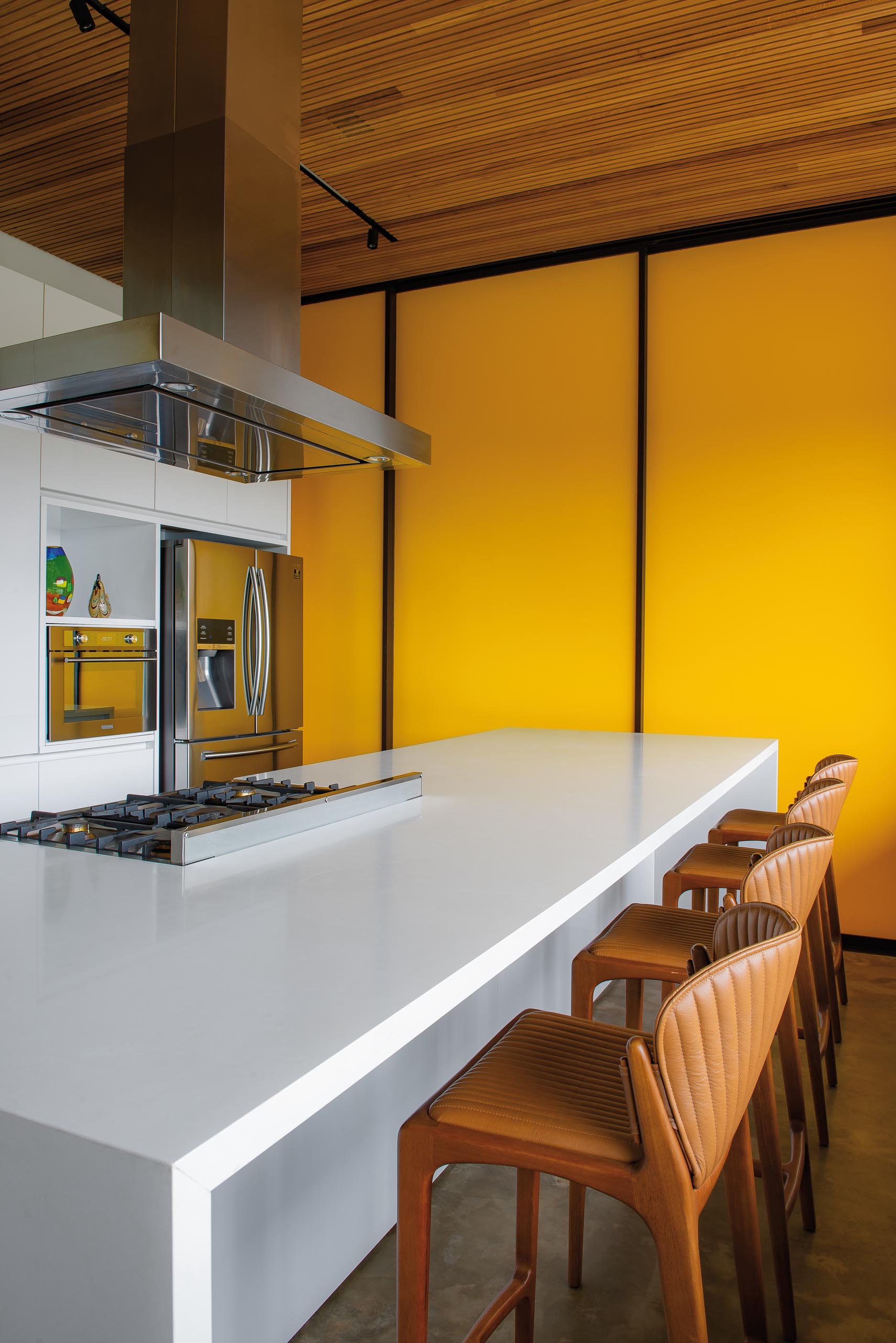 Nhà bếp hiện đại này có tủ và đảo màu trắng không có phần cứng tối giản.  Một bức tường nổi bật màu vàng tươi tạo ra một tuyên bố táo bạo và đầy màu sắc.