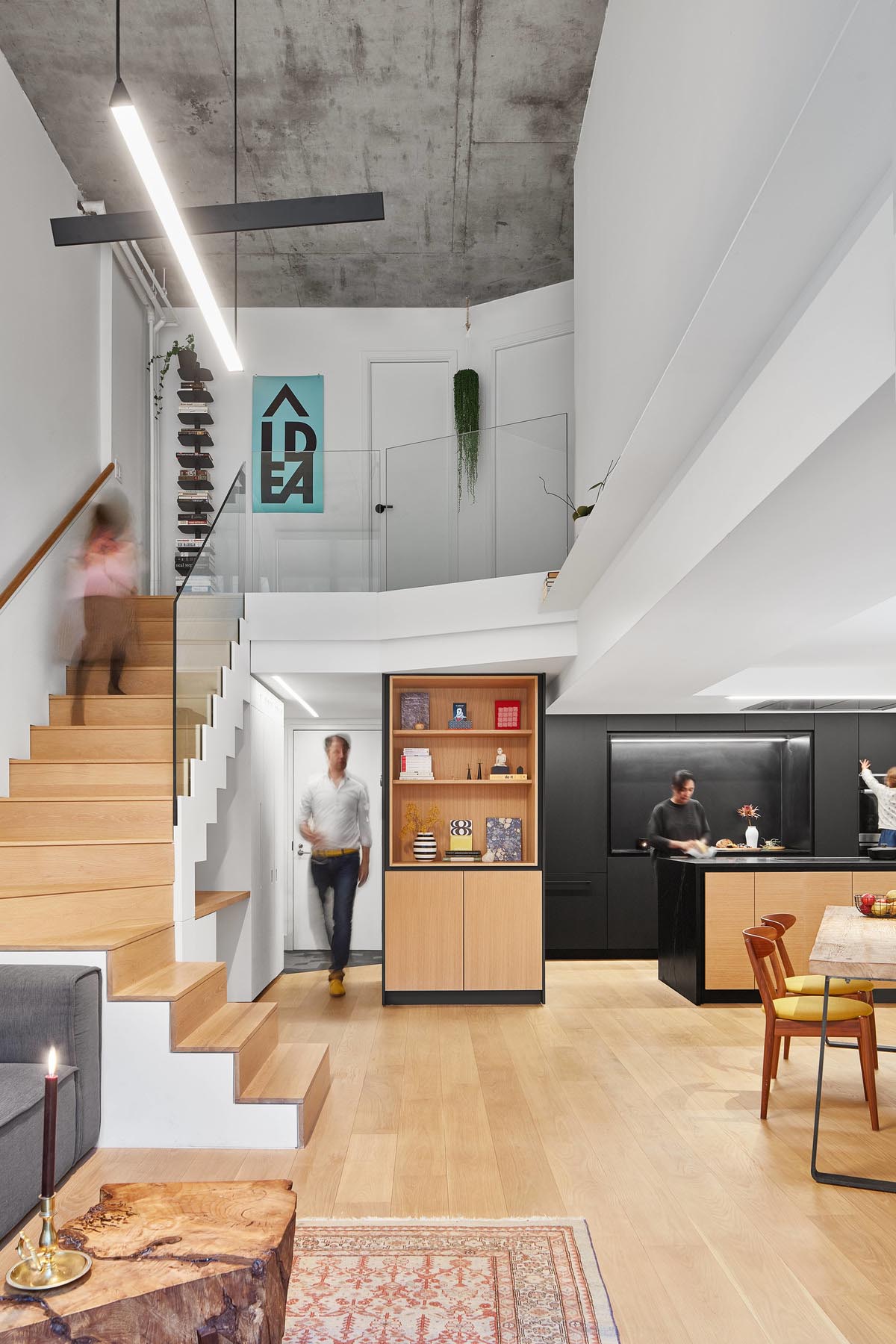 A modern loft apartment with a matte black kitchen and a built-in desk under the stairs.