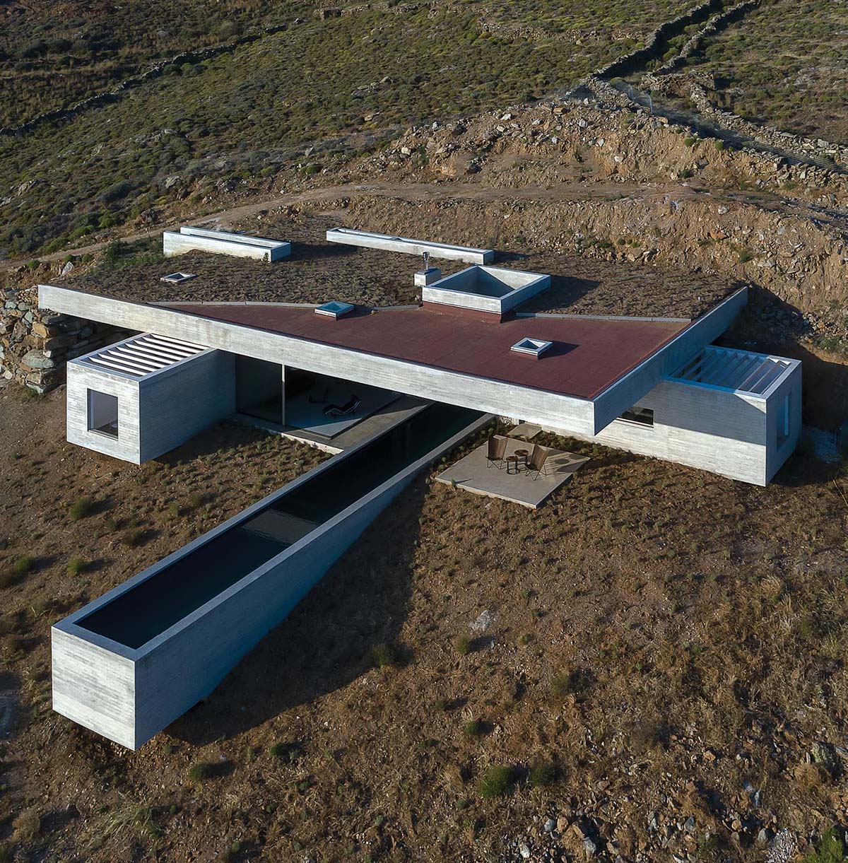 Emerging from the natural landscape as a man-made cave, this modern concrete home with a linear swimming pool, has been designed to somewhat blend in with its surroundings, with the partial green roof acting as a continuation of the hillside.