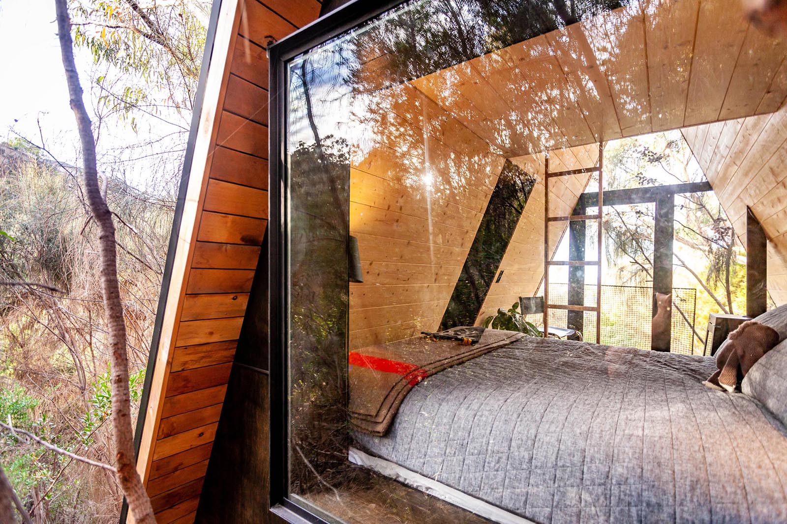 A small and modern wood-lined A-framed cabin with walls of windows at each end.