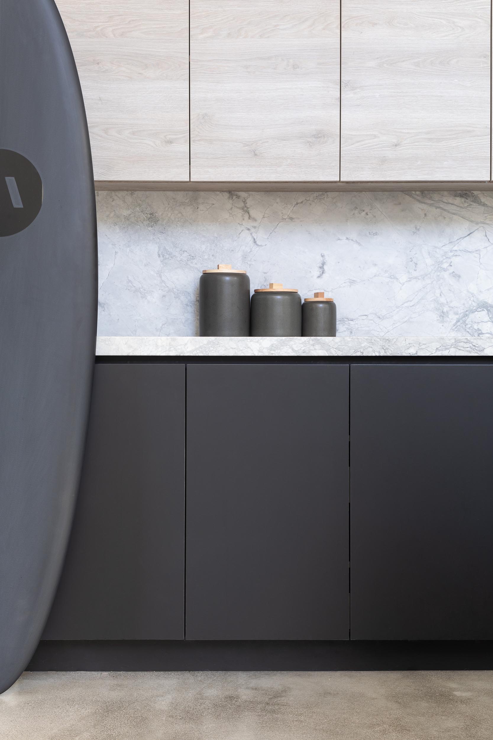 A modern kitchen with matte black lower cabinets and light wood upper cabinets.