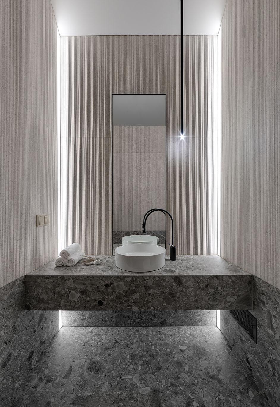 In this modern bathroom, there's simple textured walls, a minimalist light fixture, and a stone vanity and matching flooring.