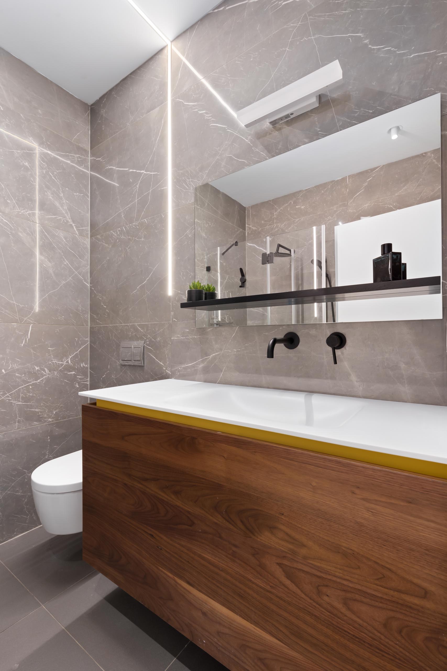 A modern bathroom with a wood vanity that includes a hint of yellow.