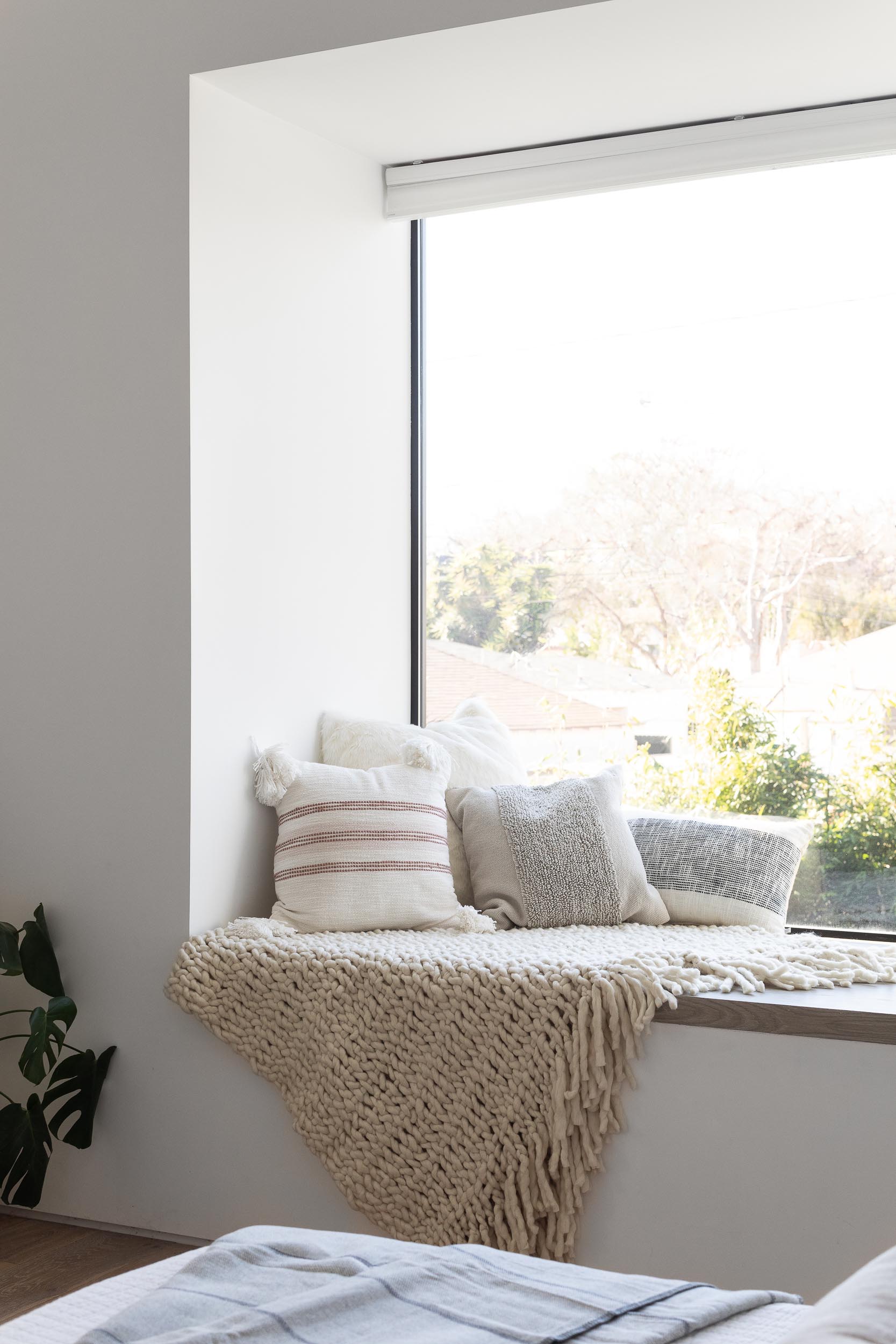 In this modern bedroom, a wood bed frame and side tables add warmth to the space, while a window seat creates a cozy place to read a book and take in the views of the yard.