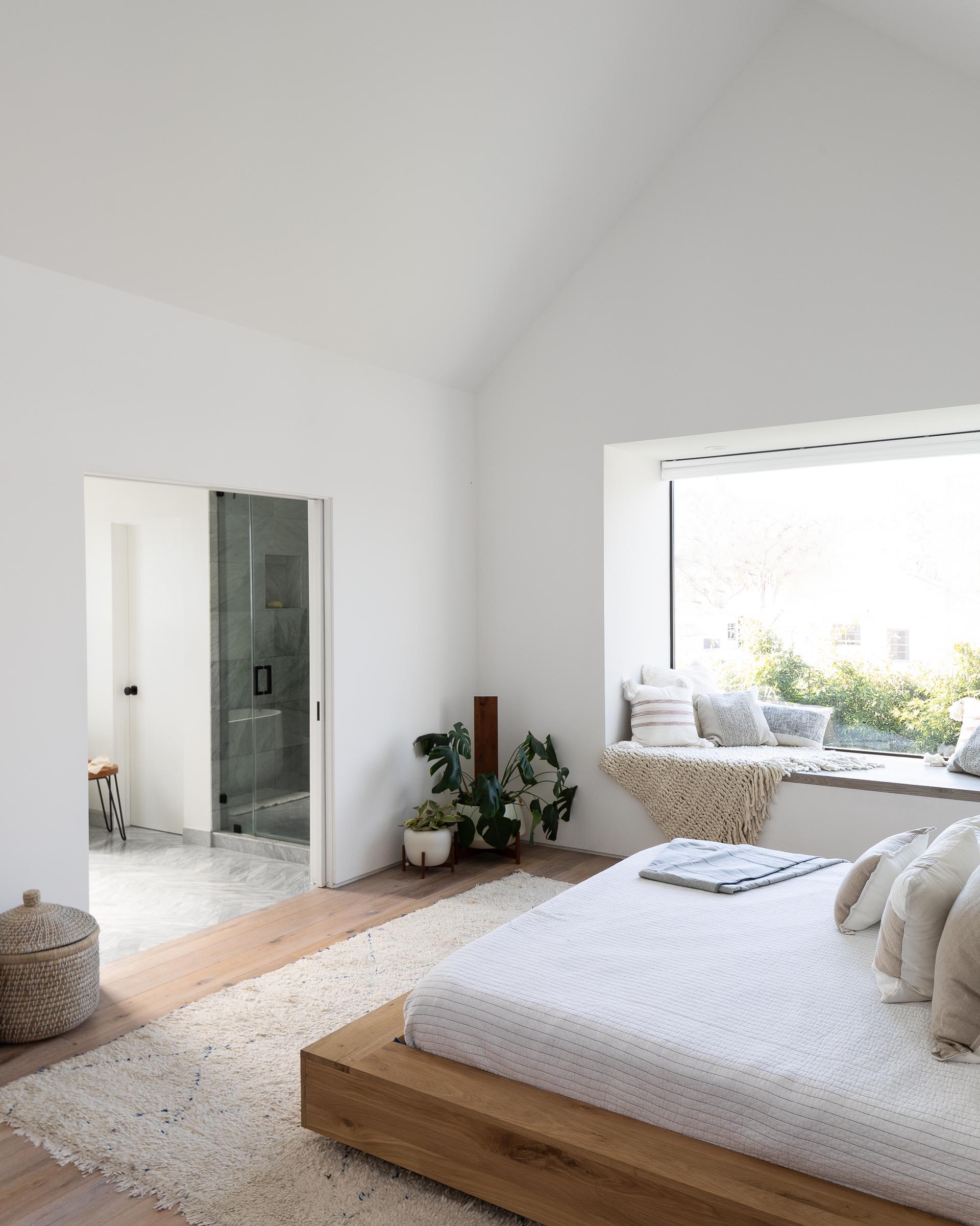 In this modern bedroom, a wood bed frame and side tables add warmth to the space, while a window seat creates a cozy place to read a book and take in the views of the yard.