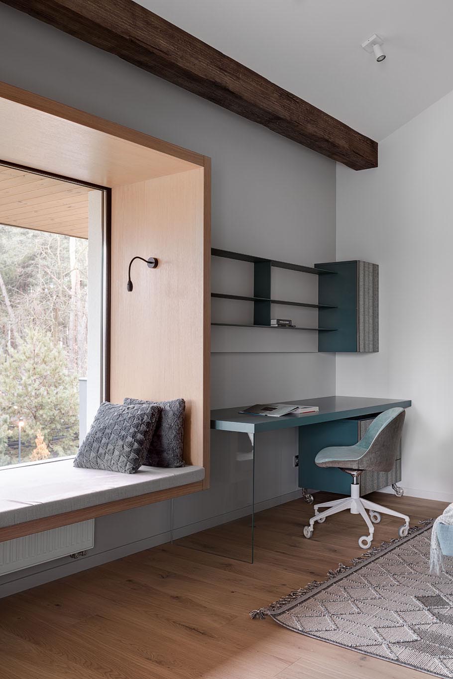 In this modern bedroom, there's a custom designed built-in window seat with views of the neighborhood. The bedroom also includes a desk with shelving above, and exposed wood beams.