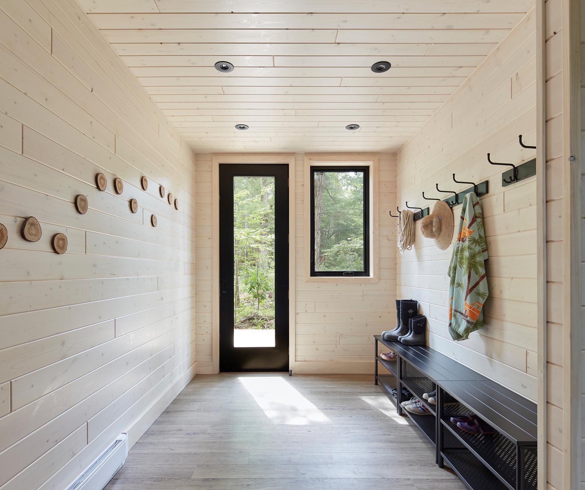 A modern entryway with light wood-lined walls and ceiling, and a matte black bench.