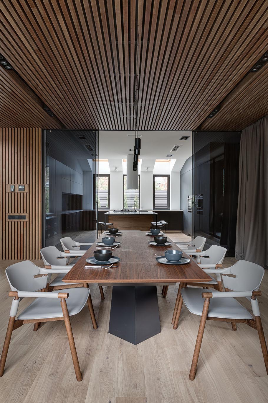 This open concept dining room has a wood slat ceiling, a wood dining table, and dining chairs that match the neutral color palette.