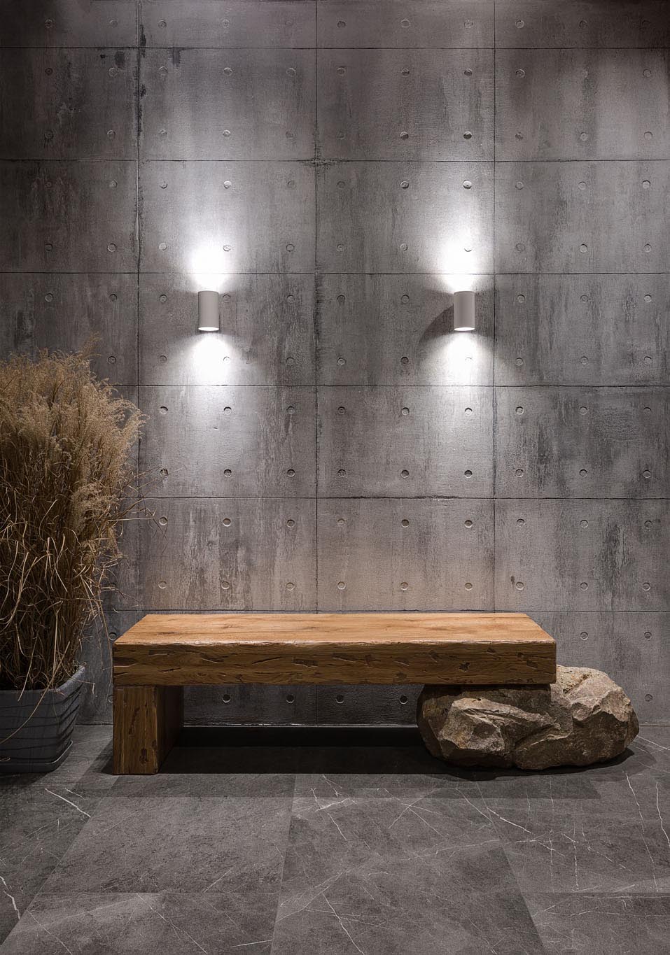 This modern entryway has an exposed concrete wall highlighted by two wall scones, and features a wood bench that rests on a boulder.