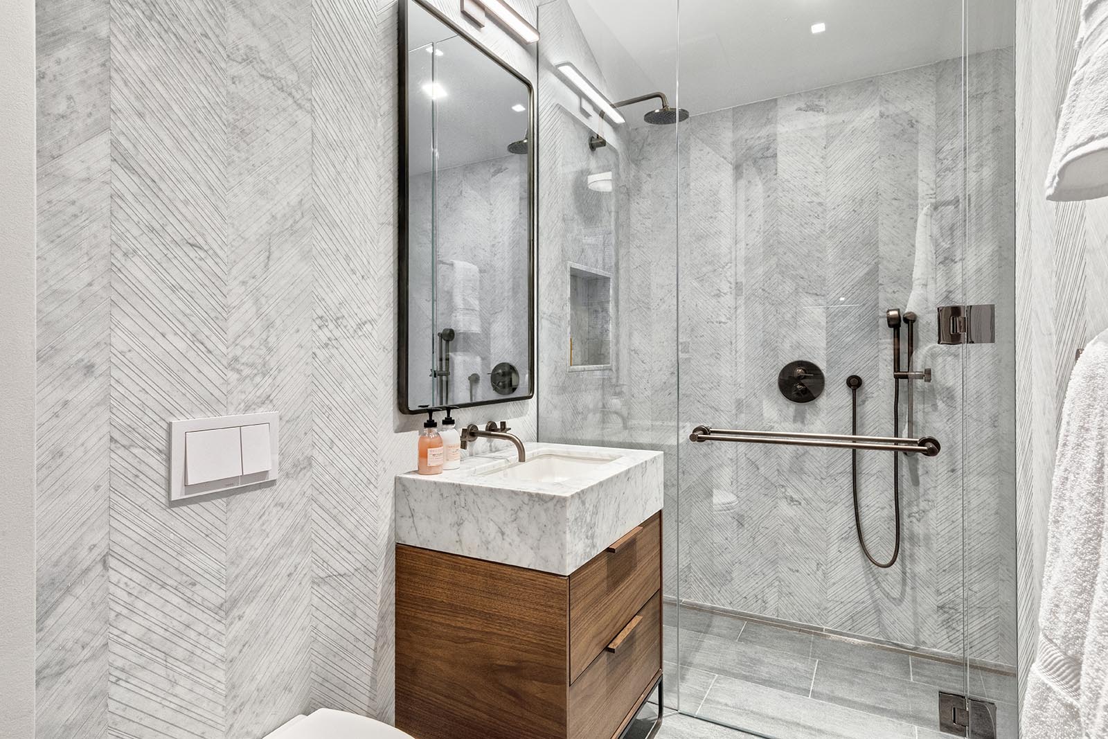 In this modern bathroom, there's floor-to-ceiling gray stone walls, a wood vanity, and a glass enclosed shower.