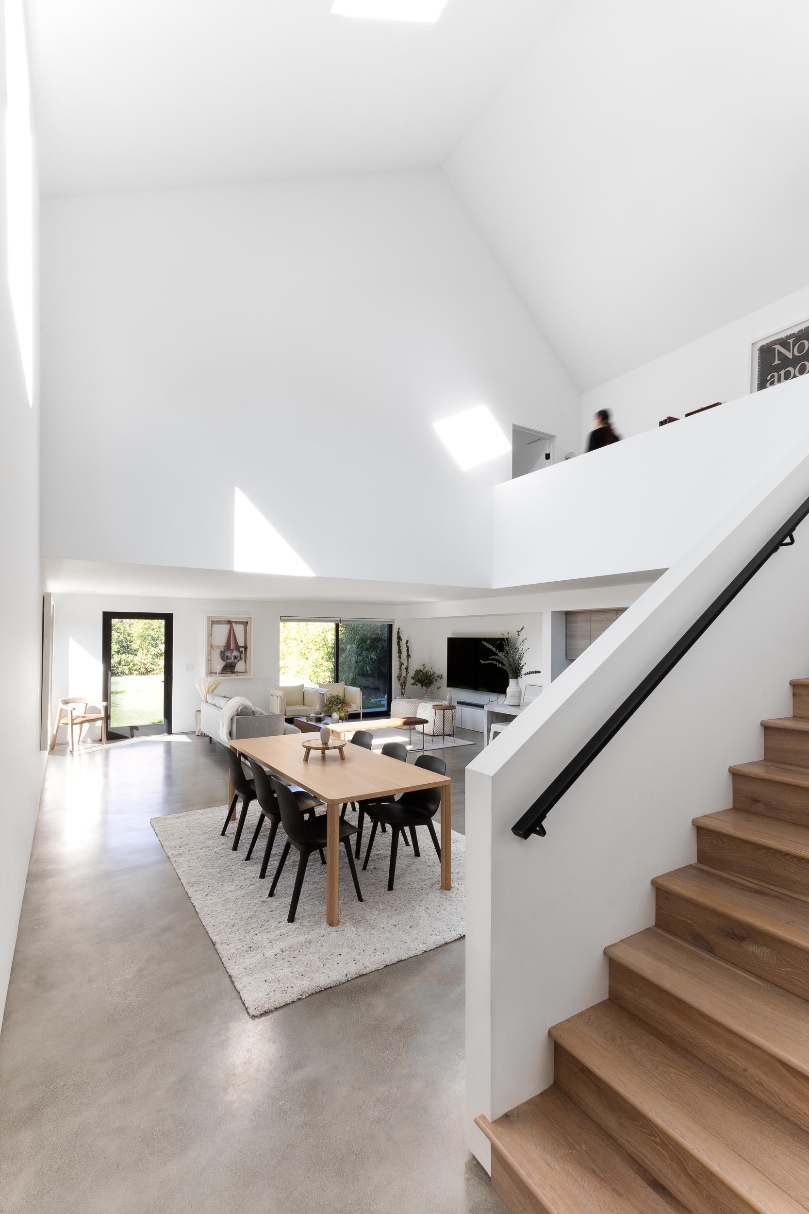 Inside this modern home, there's an open floor plan with the living room, dining room, and kitchen all sharing the same space. Also included are high ceilings, concrete floors, and bright white walls.