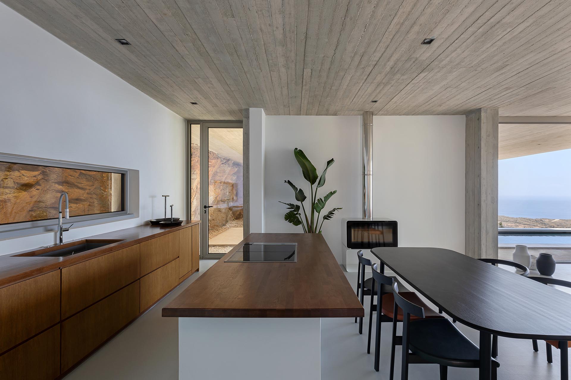 A concrete home built into the hillside, has an open living room, dining room, and kitchen, with the backsplash providing a view of the natural rocks.