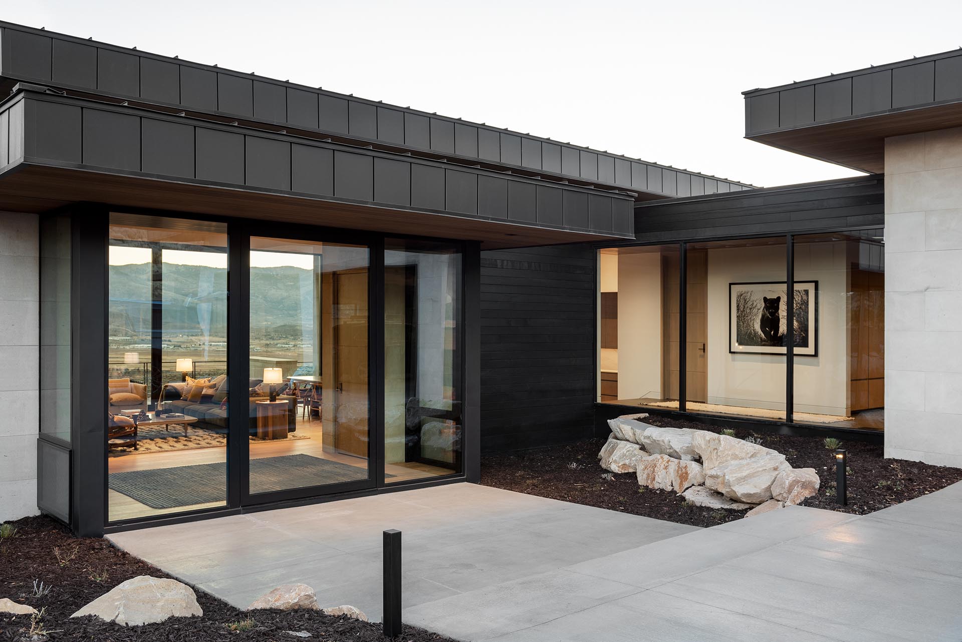 The exterior of this home includes exposed concrete and black siding, while a glass front door gives a glimpse of the interior.