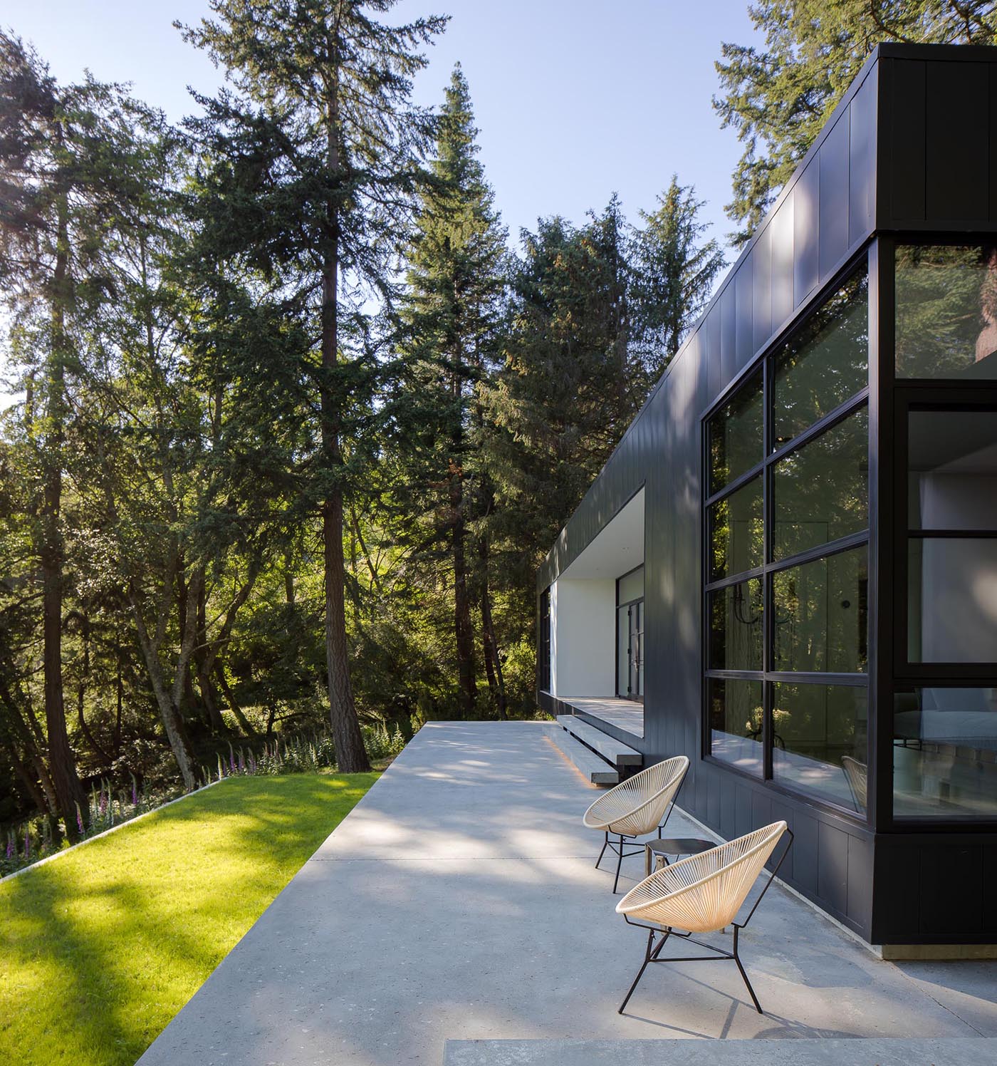 Black framed doors open the interior spaces of this modern home to the rear concrete terrace.