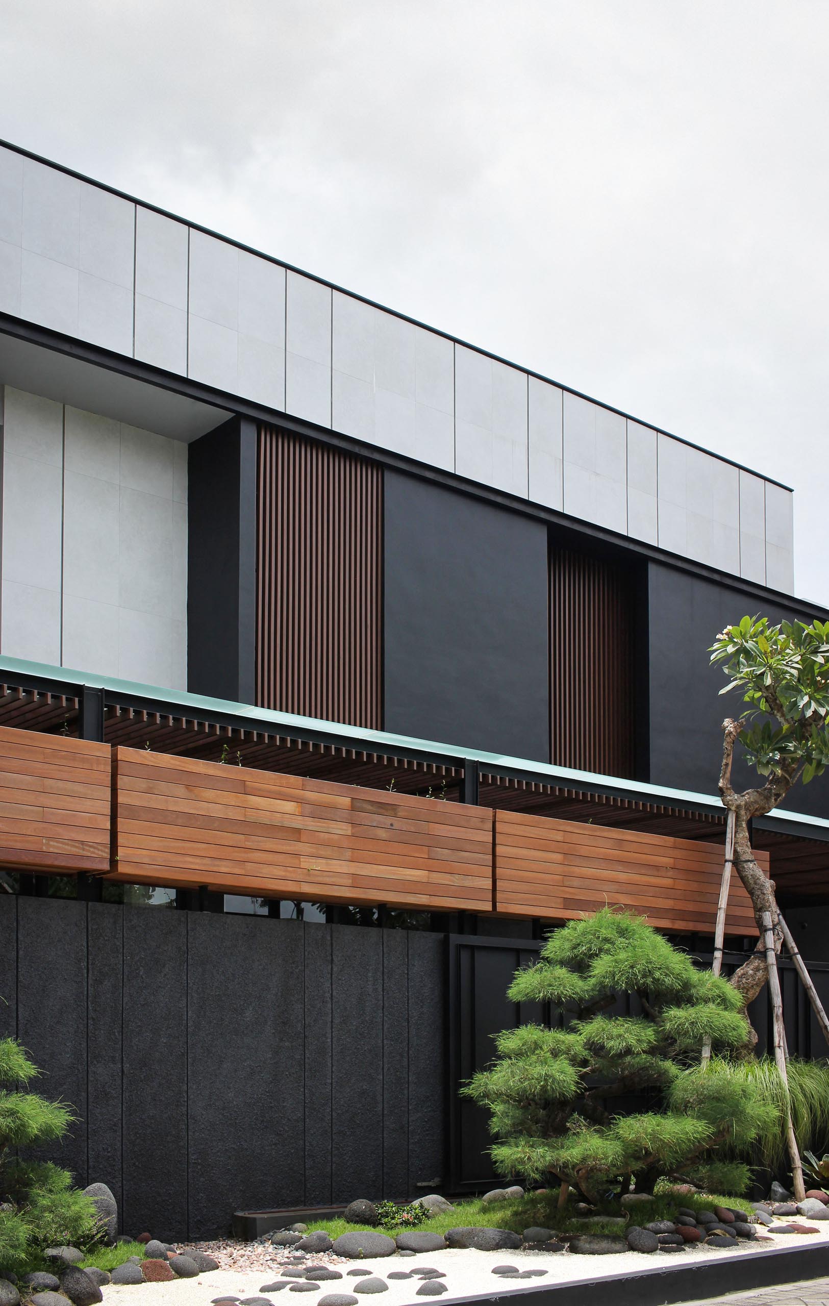 This Zen garden has a dark matte black and wood fence as a backdrop, and includes ornamental trees, white pebbles, gray stones, and small sections of grass.