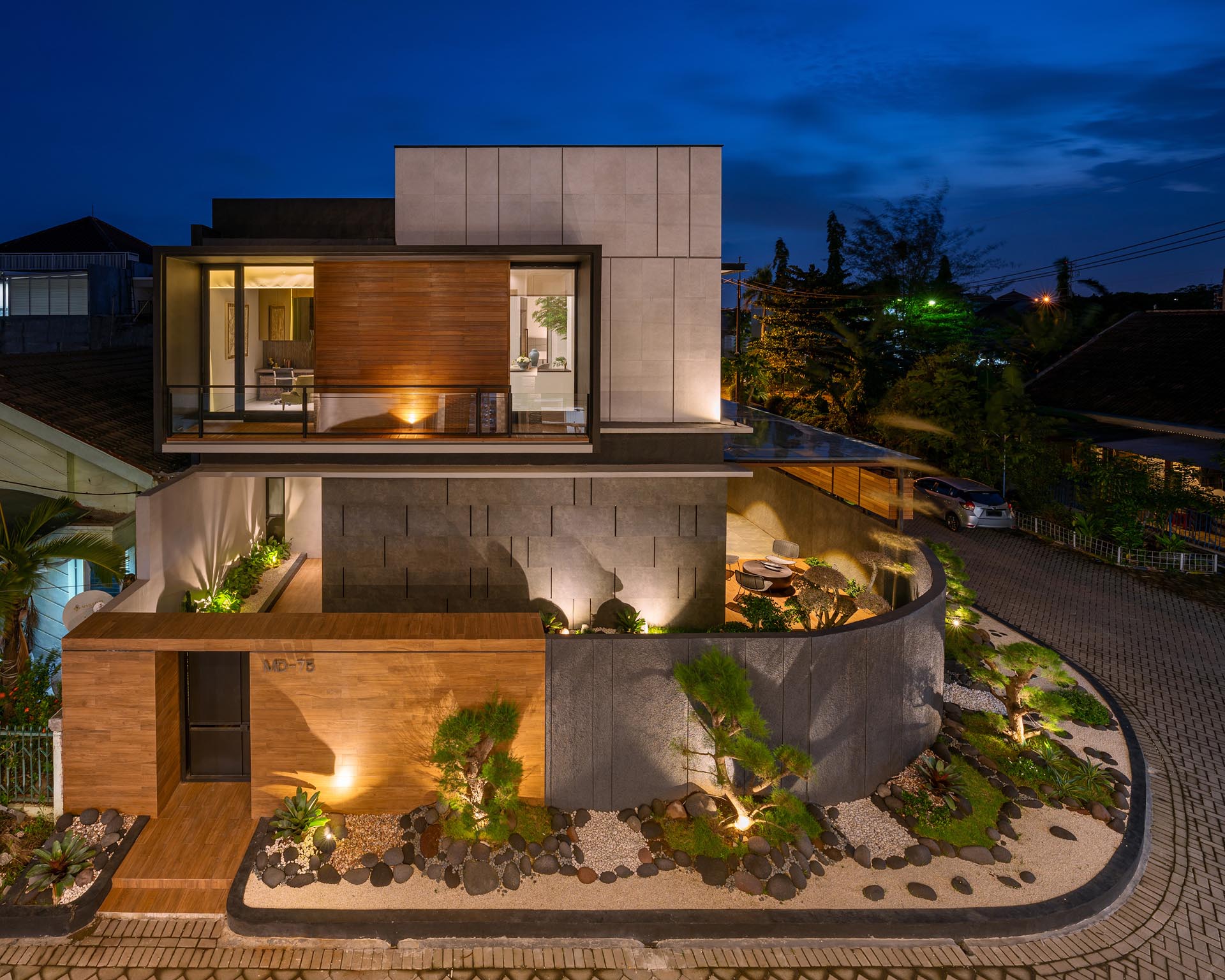 This Zen garden creates modern  curb appeal for a corner lot, and has a dark matte black and wood fence as a backdrop. It also includes ornamental trees, white pebbles, gray stones, and small sections of grass.