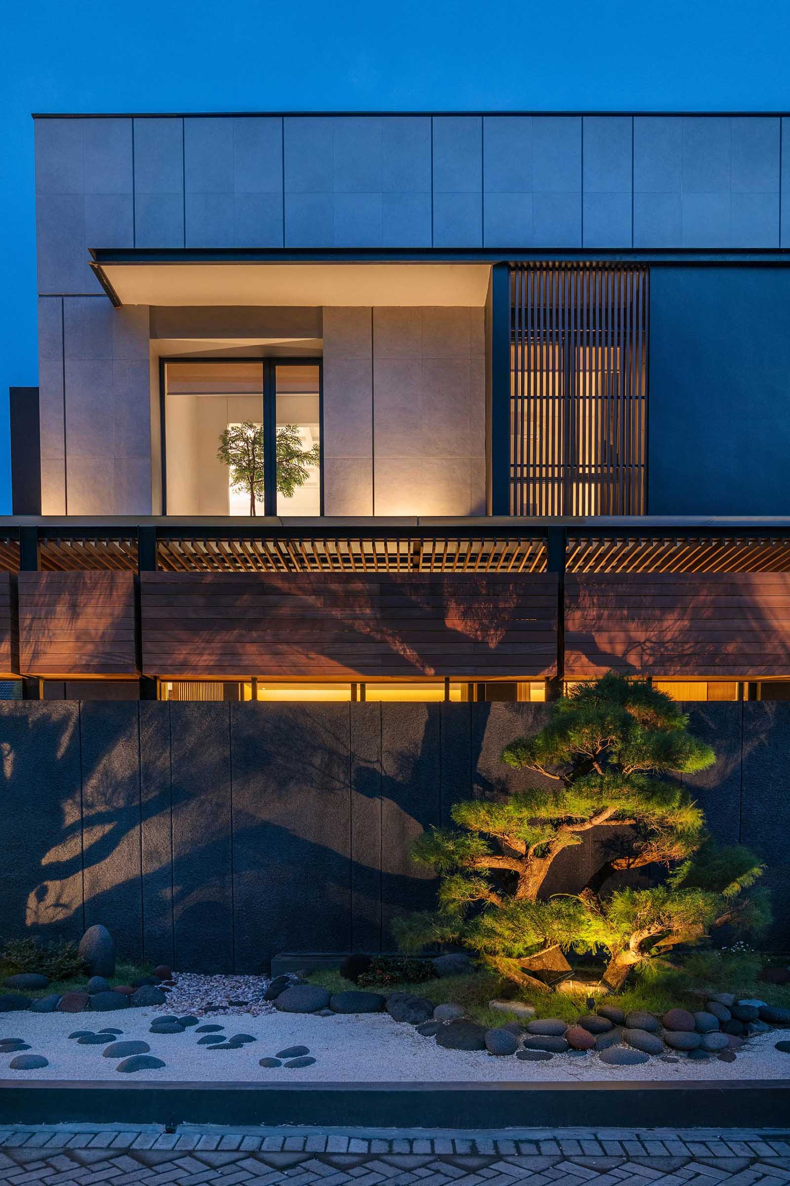 Lighting has been installed within this modern Zen garden, which allows the plants to be showcased at night, casting shadows onto the fence, and adding extra light to the neighborhood.