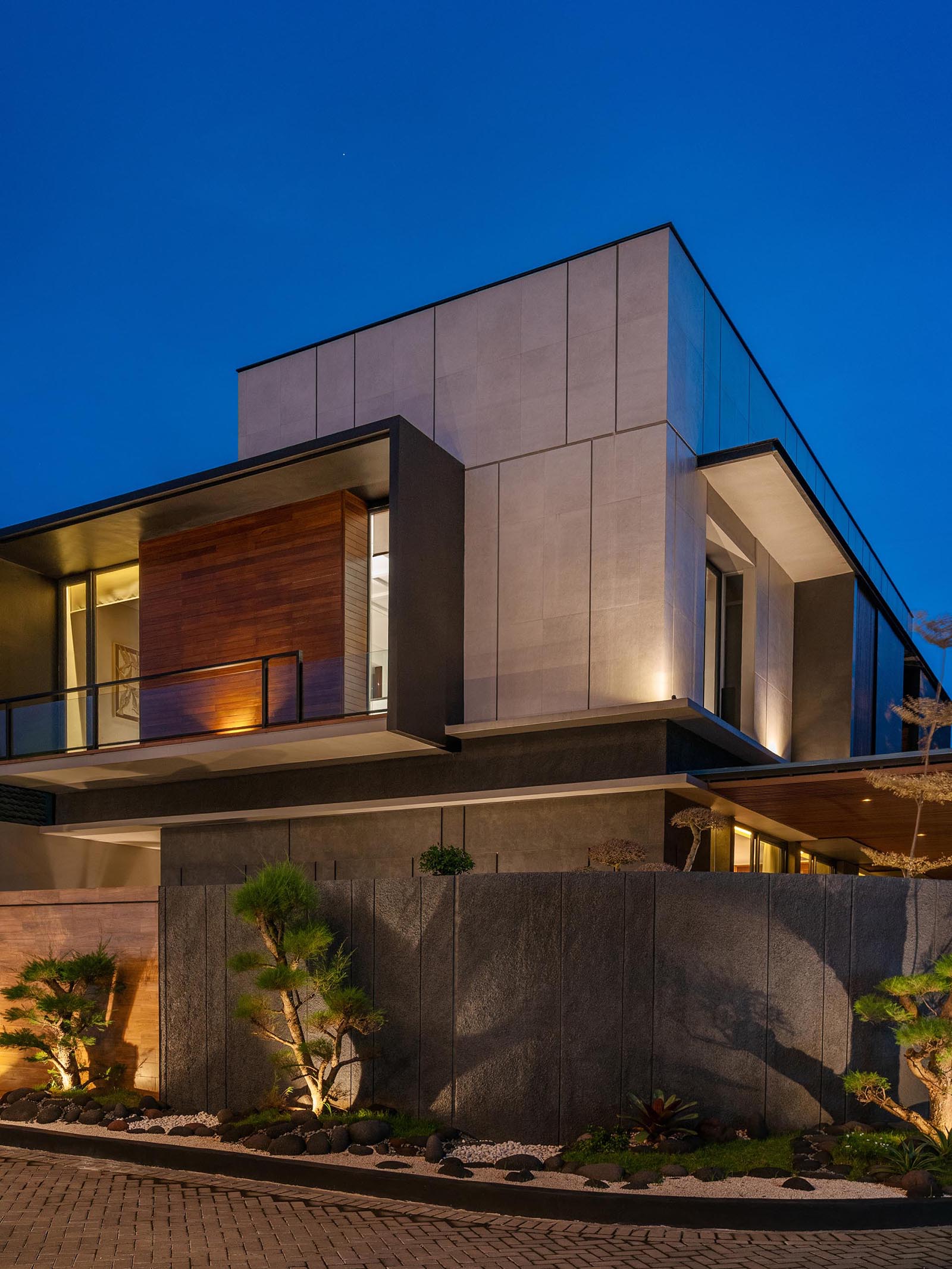 Lighting has been installed within this modern Zen garden, which allows the plants to be showcased at night, casting shadows onto the fence, and adding extra light to the neighborhood.