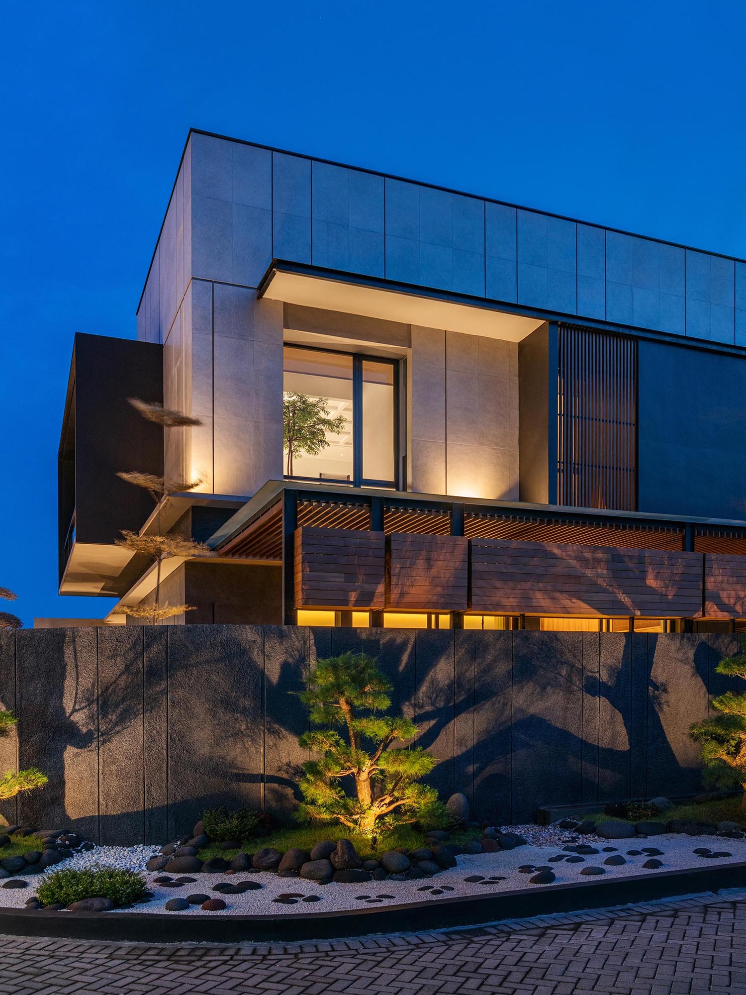 Lighting has been installed within this modern Zen garden, which allows the plants to be showcased at night, casting shadows onto the fence, and adding extra light to the neighborhood.