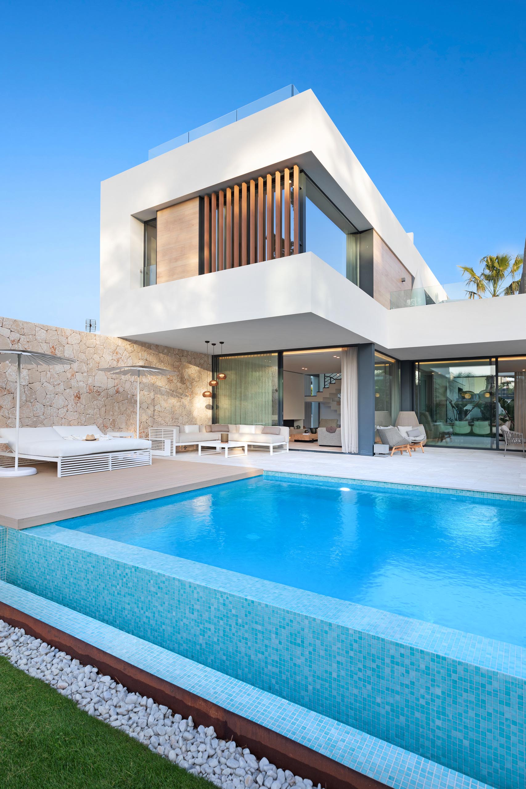 A modern home with a swimming pool, stone walls, a deck, and partially covered patio.