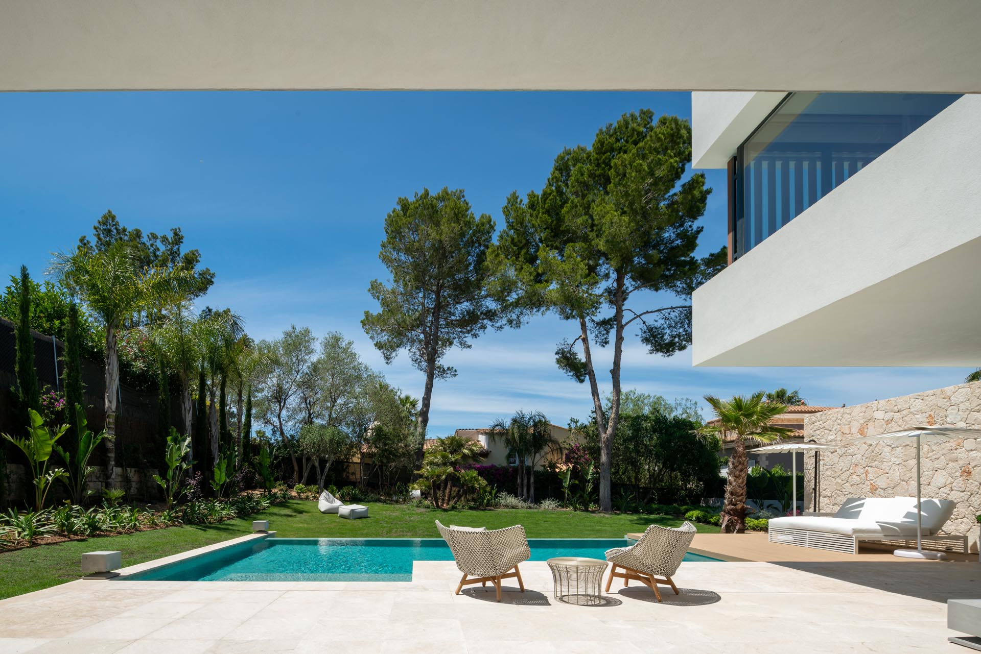 The deck and patio of this modern home look out towards the swimming pool and yard, which is lush with grass, shrubs, and trees.