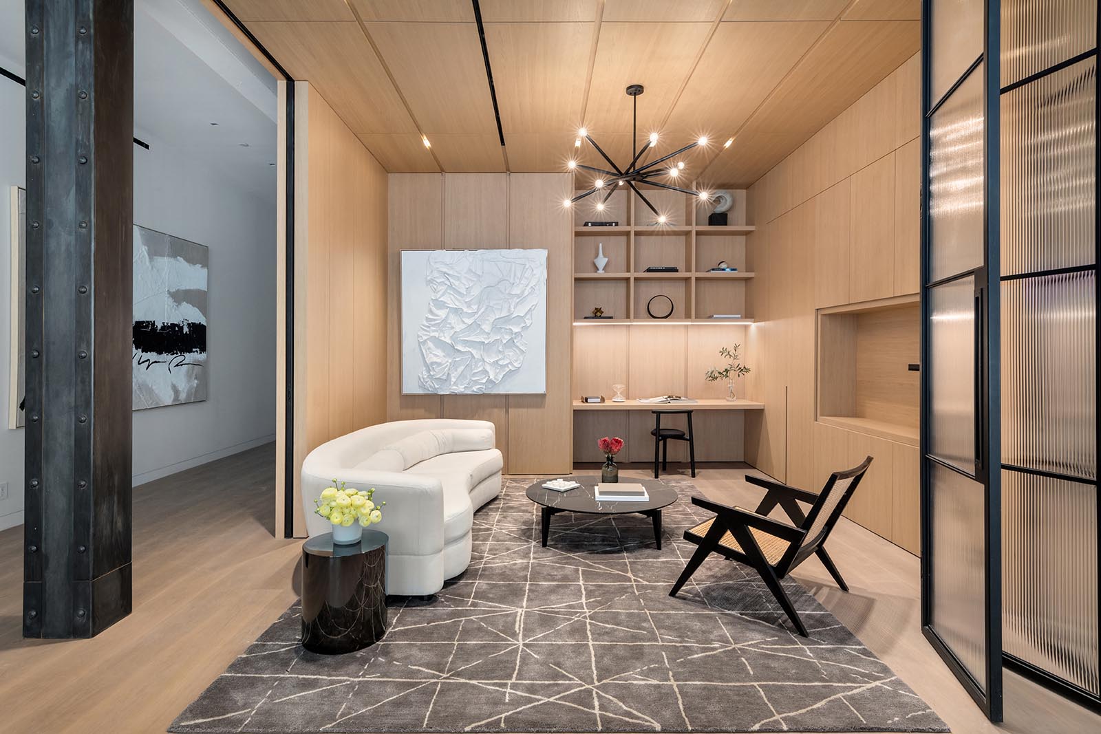 A spacious library with a built-in desk, is clad in millwork that was made in Italy by Canova, and includes floor-to-ceiling glass and steel casement folding doors, creating an open and versatile additional living space.