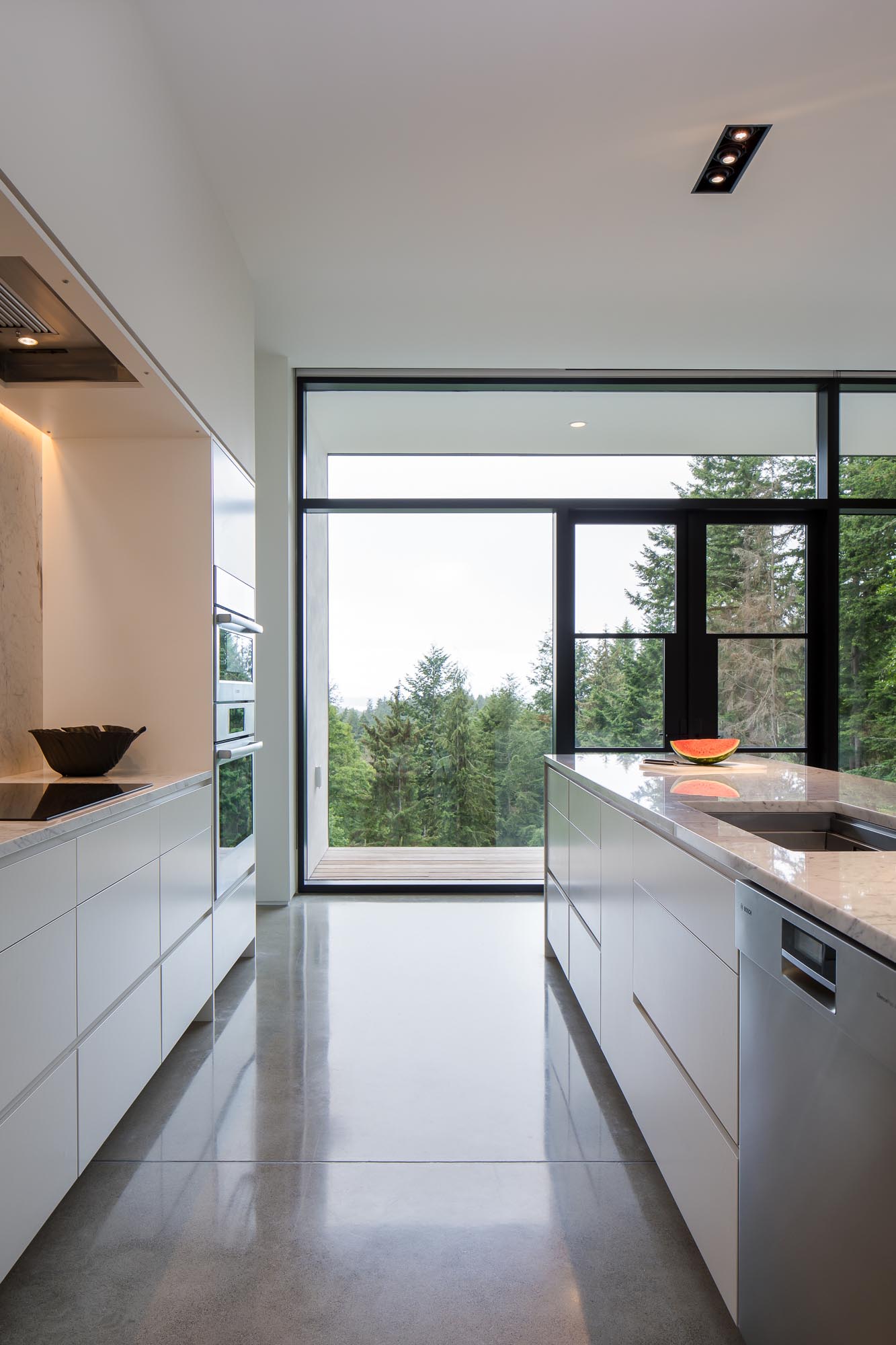 Nhà bếp hiện đại với tủ màu trắng tối giản, mặt bàn bằng đá cẩm thạch Carrera và sàn bê tông màu xám.