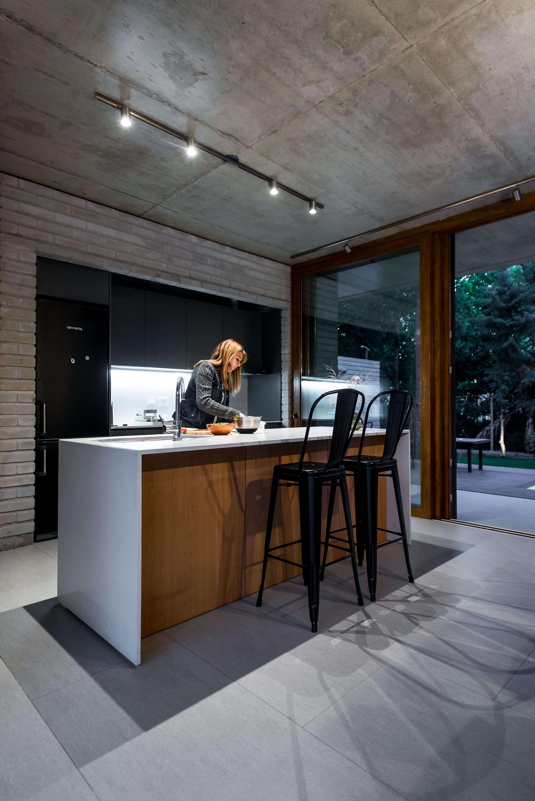 A modern kitchen with exposed concrete, black cabinets, a white island and wood accents.