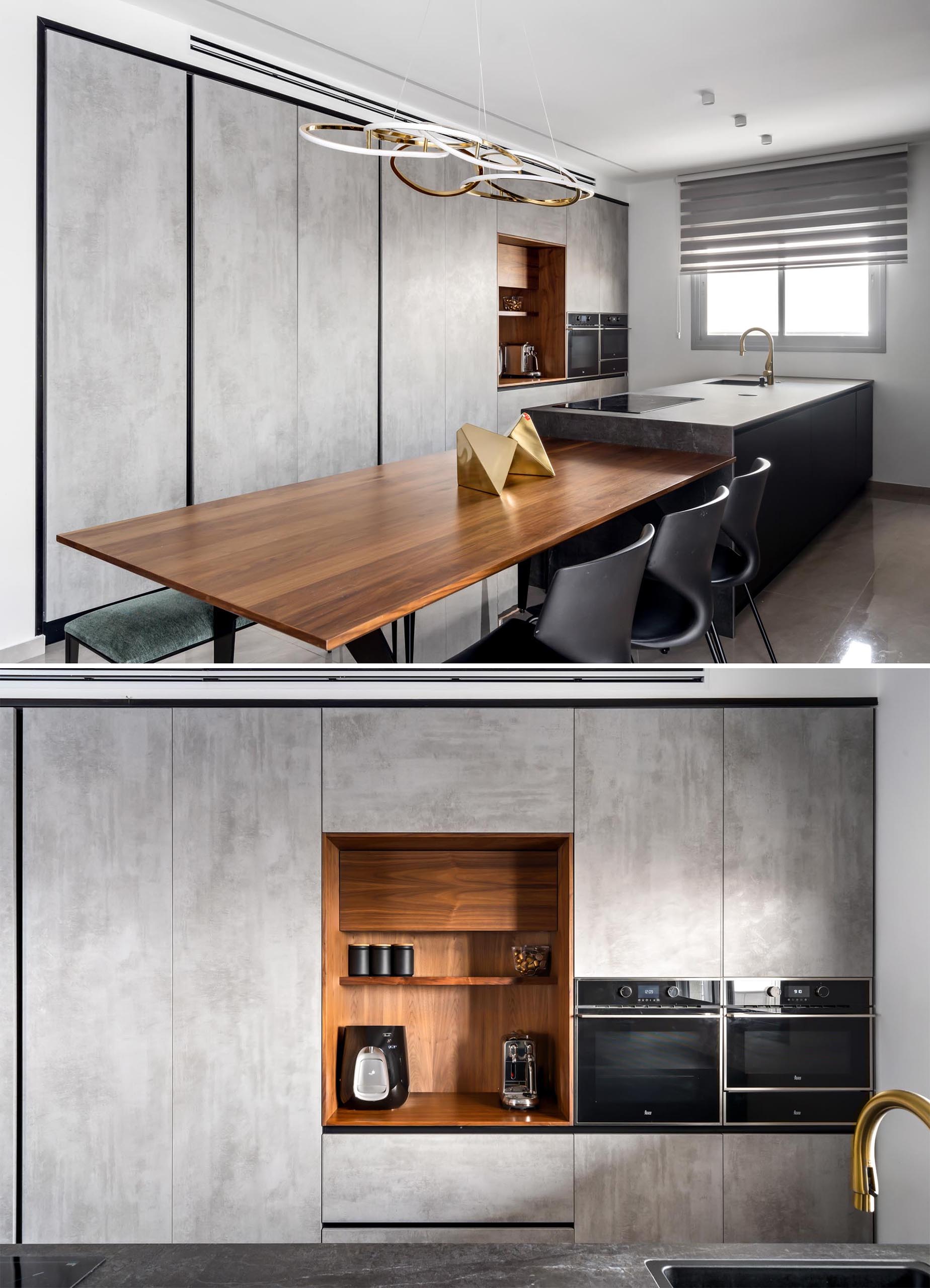 In this modern kitchen, minimalist hardware free gray cabinets line the wall, while a wood niche is home to a coffee machine and open shelving. The kitchen peninsula incorporates a wood dining table, complementing the other wood elements found nearby.