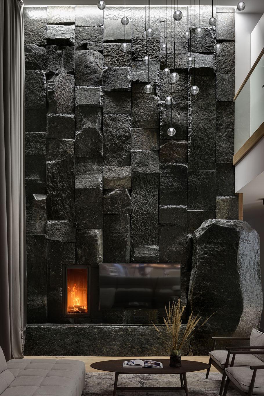 A large, dark, and monumental natural stone boulder wall that's used as a backdrop for the fireplace and television.