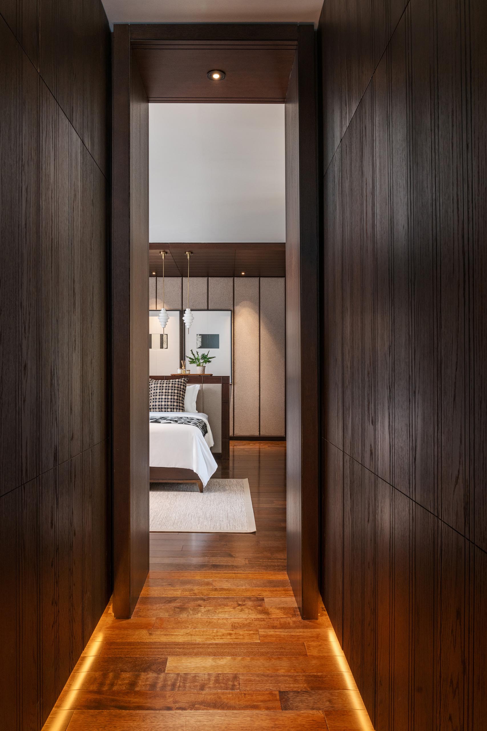 A hallway lined with dark wood cabinets and hidden lighting provides access to the primary bedroom.