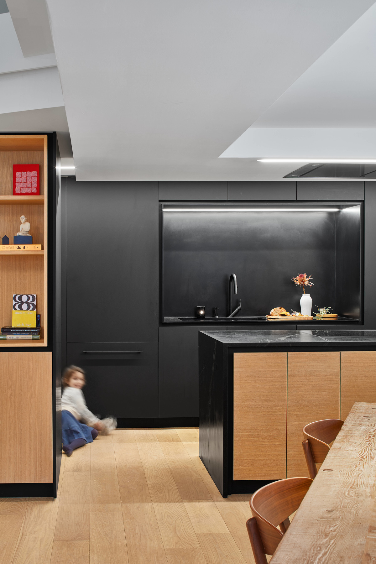 A modern matte black kitchen with hardware free cabinets and a large island with wood accents.