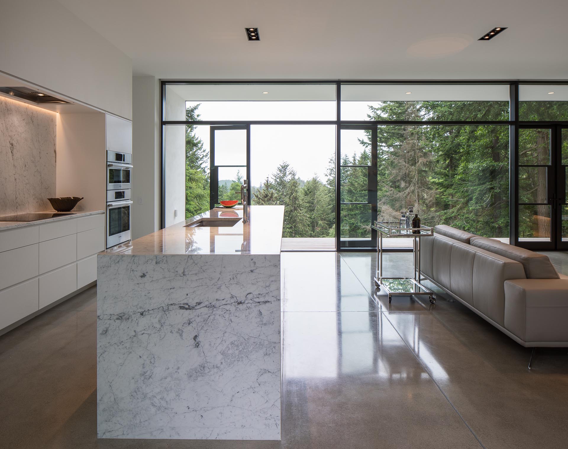 A modern kitchen with minimalist white cabinets, Carrera marble countertops, and gray concrete flooring.