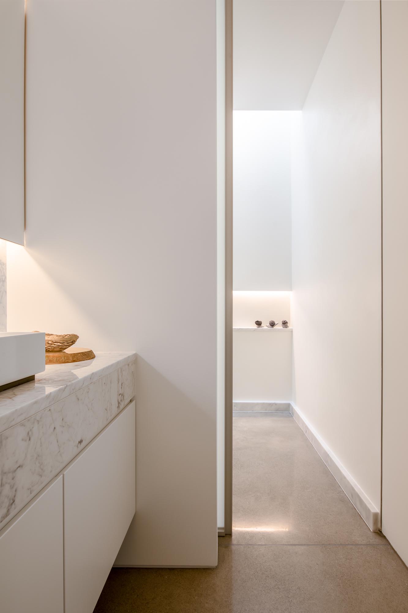 This modern en-suite bathroom has a backlit mirror, a floating vanity, and a walk-in shower with a shelving niche.